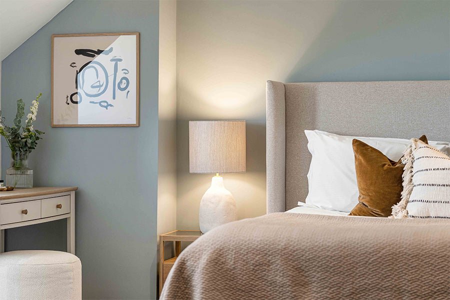 Tranquil master bedroom interior with upholstered headboard, soft taupe bedding, ceramic bedside lamp, abstract wall art, and sage green accent wall – styled by Iroka Interiors.