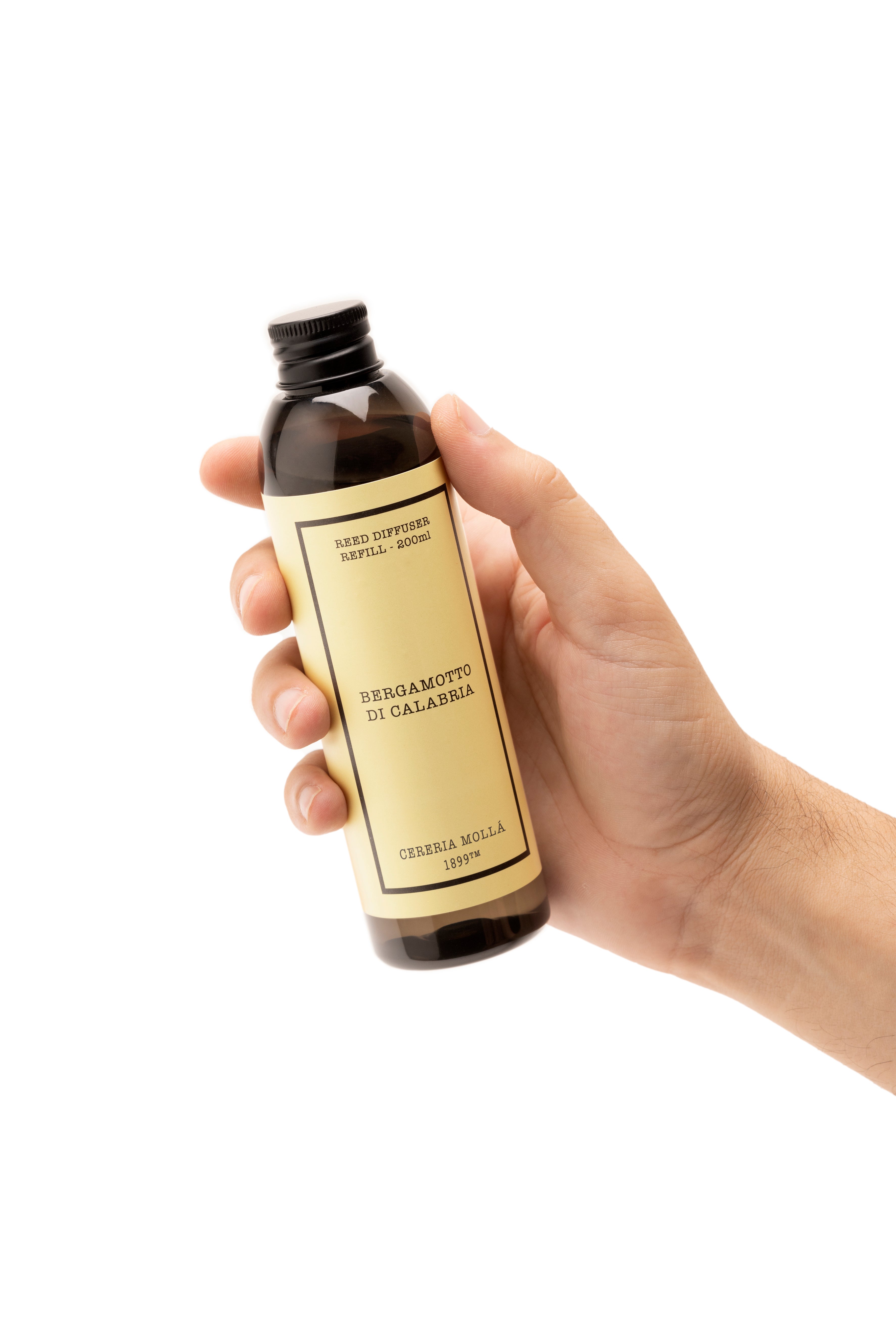 A hand holding a dark amber glass bottle with a black cap and a beige label. The label features black text reading 'bergamotto di calabria'