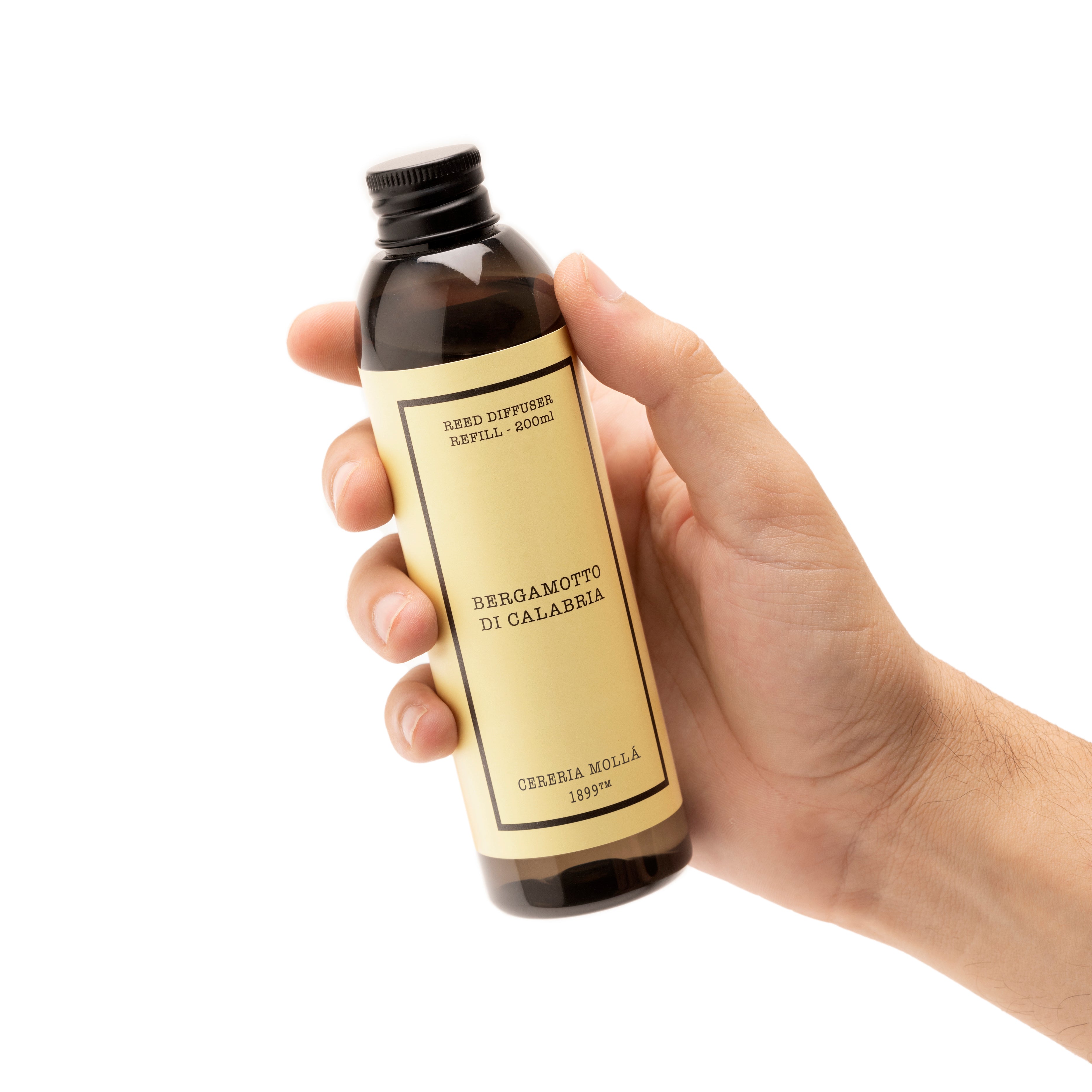 A hand holding a dark amber glass bottle with a black cap and a beige label. The label features black text reading 'bergamotto di calabria'