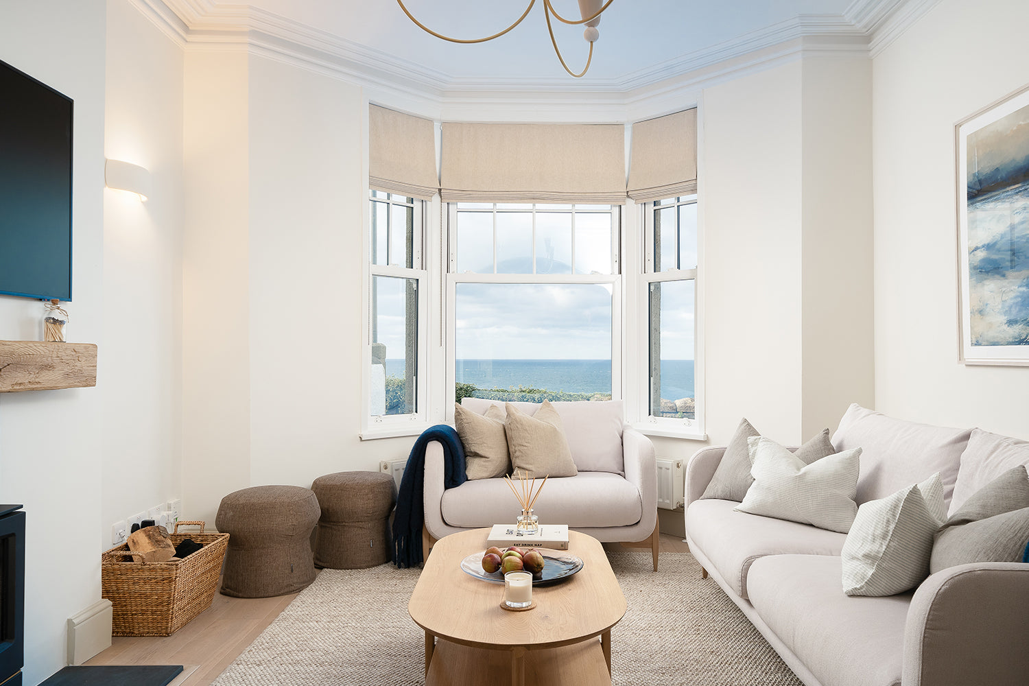 Bright coastal living room designed by Iroka Interiors at Seaglass View, featuring neutral sofas, a natural wood coffee table, textured woven rug, and a panoramic sea view through a large bay window.