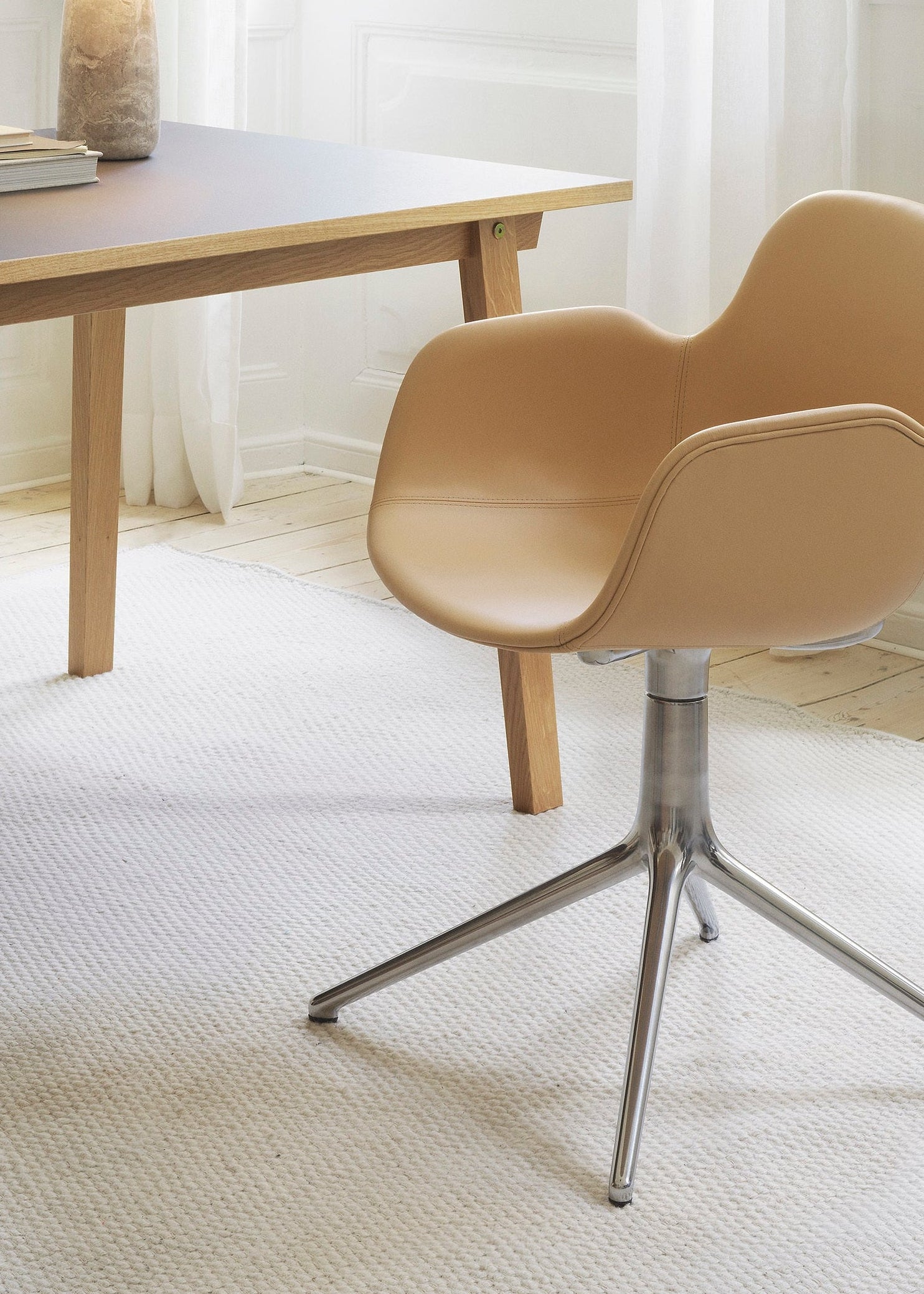 Beige chair with metal legs in front of a wooden table on a light-colored floor.