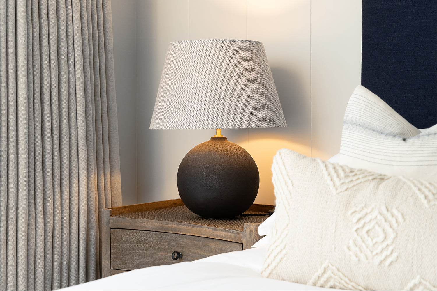 Close-up of a luxury bedside table with sculptural ceramic lamp, soft pleated curtains, and crisp white bedding – bedroom styling by Iroka Interiors.