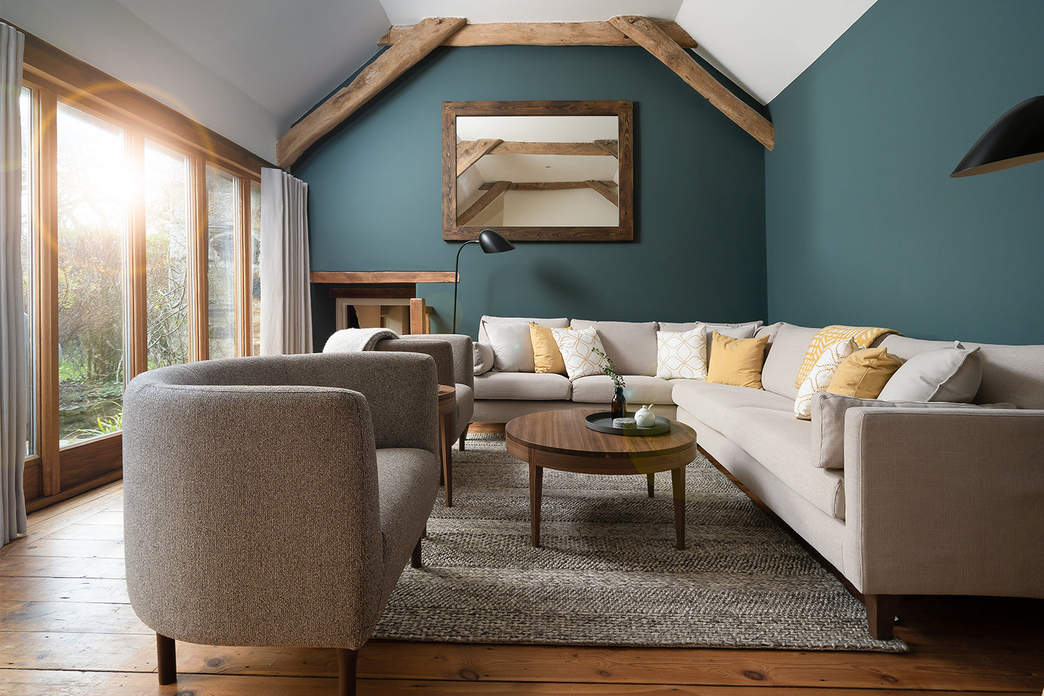 Coastal-inspired living room with pitched ceiling, teal feature wall, neutral corner sofa and yellow accents – styled interior in Port Isaac by Iroka.