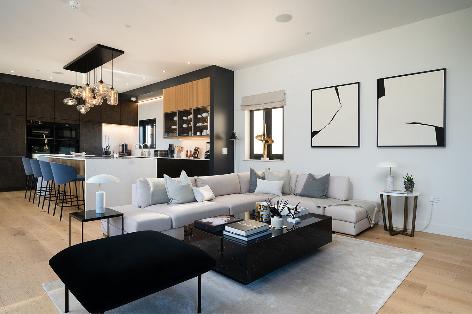 Stylish living area and kitchen in Pentire Penthouse, Newquay – featuring monochrome abstract wall art, plush seating, and a modern kitchen design with statement lighting by Iroka Interiors.