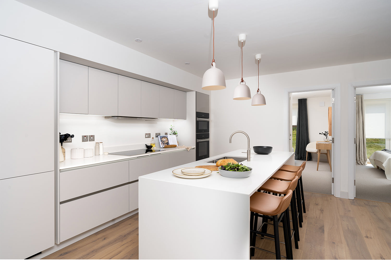 Contemporary white kitchen at Azure showhome, Carbis Bay - features a waterfall island with bar stools, integrated appliances, pendant lighting, and minimalist cabinetry - styled by Iroka Interiors.