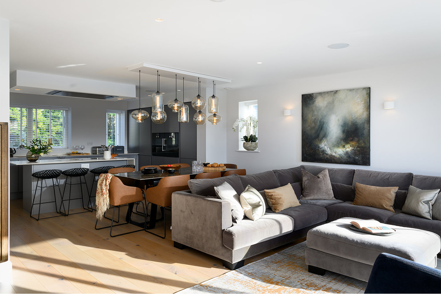 Open-plan living, dining and kitchen space at Paradise View featuring modern pendant lighting, taupe velvet corner sofa, abstract wall art, and sleek monochrome cabinetry – interior design by Iroka.