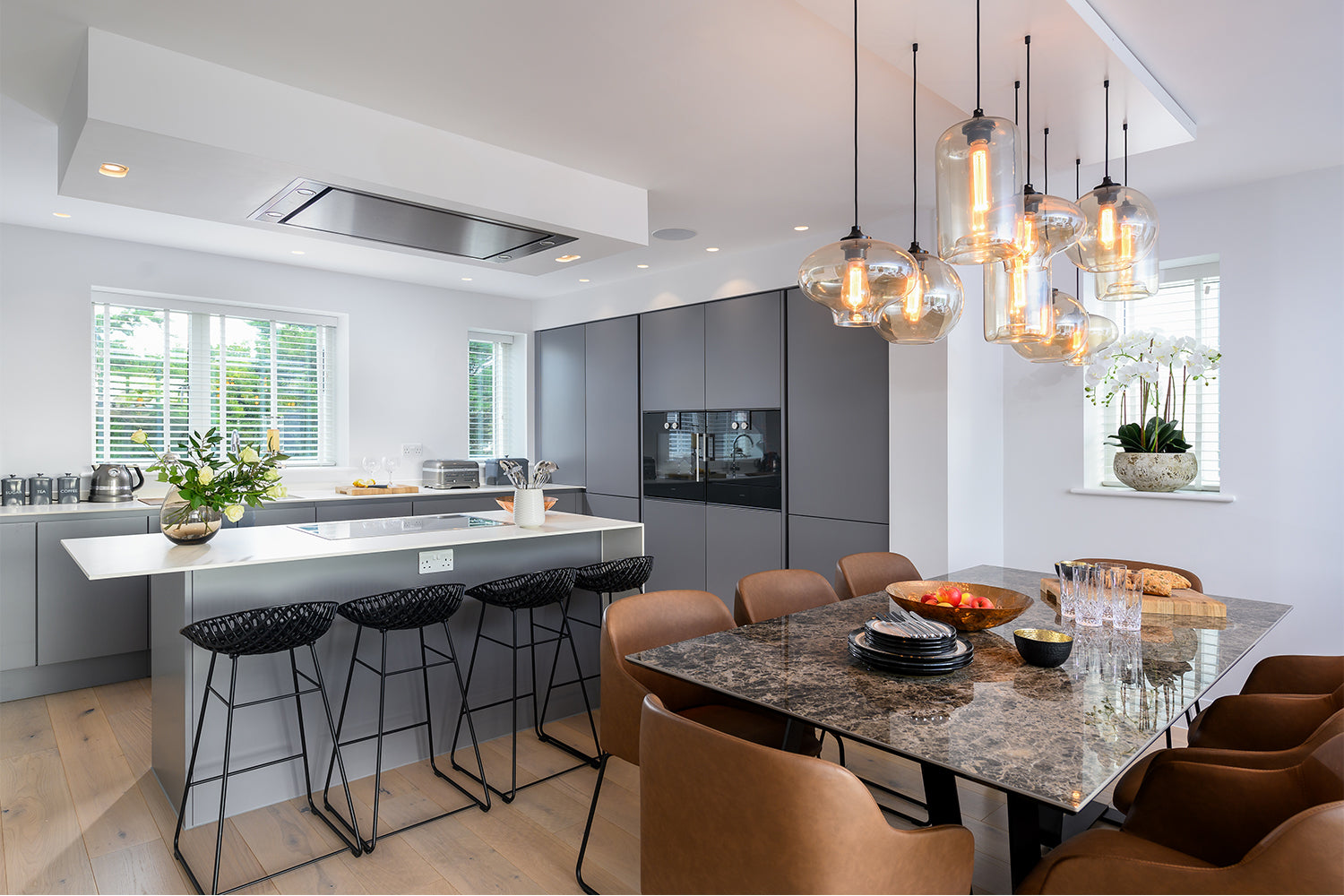 Contemporary kitchen and dining area at Paradise View, featuring a marble island with black bar stools, matte grey cabinetry, bronze leather dining chairs, and designer pendant lighting – styled by Iroka Interiors.