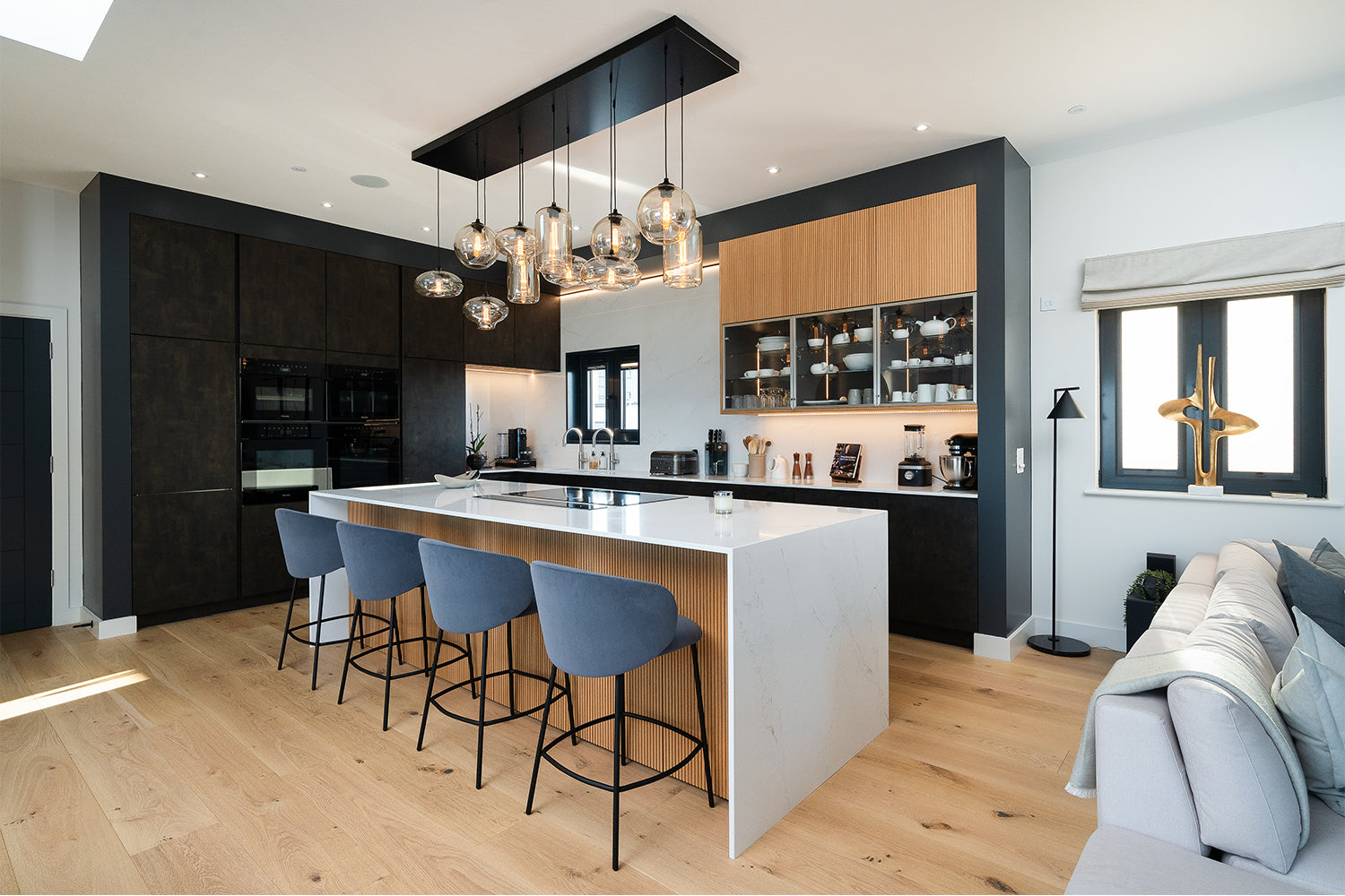 Modern kitchen design in Pentire Penthouse, Newquay – featuring a marble waterfall island, contemporary pendant lighting, navy bar stools, and a sleek black and wood cabinetry scheme by Iroka Interiors.
