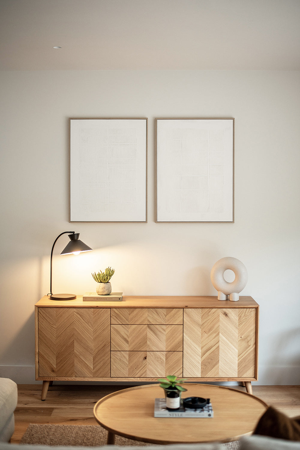 Modern living room with a light oak herringbone sideboard, black reading lamp, sculptural decor and minimal framed artwork above, styled with warm neutral tones and natural textures.