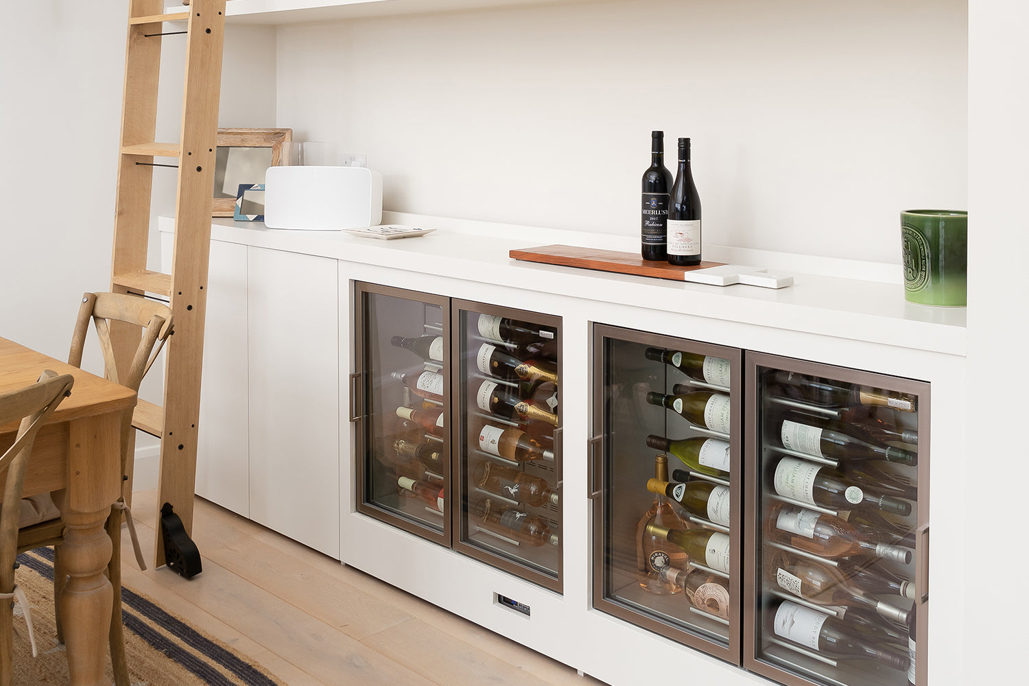 Stylish wine fridge and bar area with dual glass-fronted coolers, minimalist shelving and natural wood accents – interior styling by Iroka.
