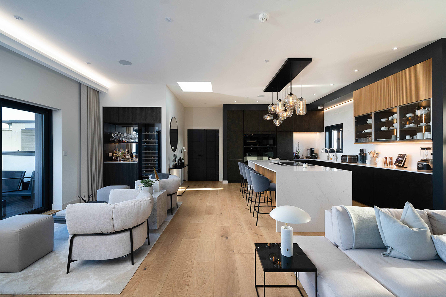 Luxury open-plan kitchen and living area at Pentire Penthouse, Newquay – featuring a waterfall-edge marble island, statement pendant lighting, bespoke black and oak cabinetry, and contemporary soft seating by Iroka Interiors.