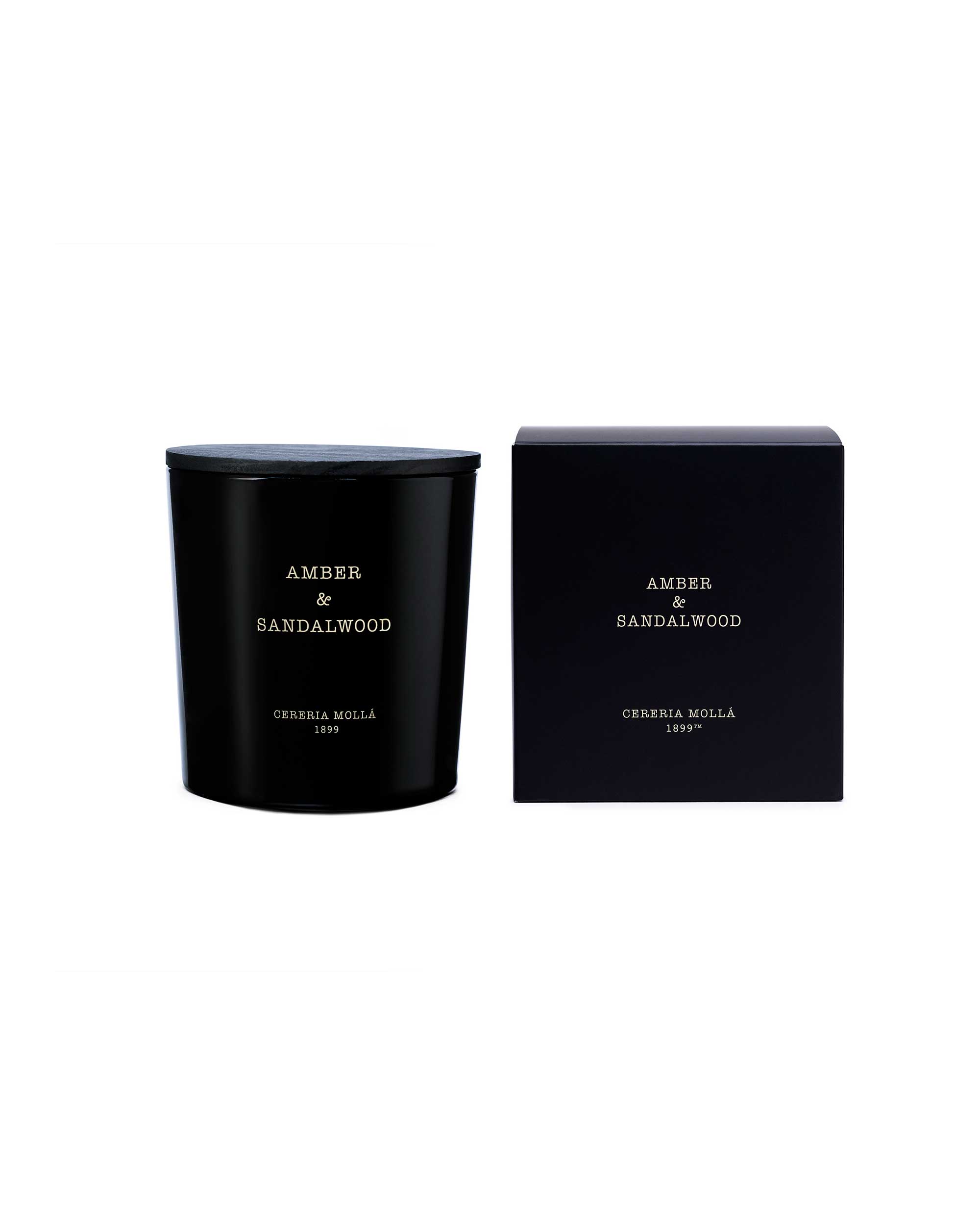 A black glass candle jar with a matching black lid sits next to its black packaging box on a plain white background. The text on both items reads 'AMBER & SANDALWOOD' and 'CERUSA MOTTA 1995'.