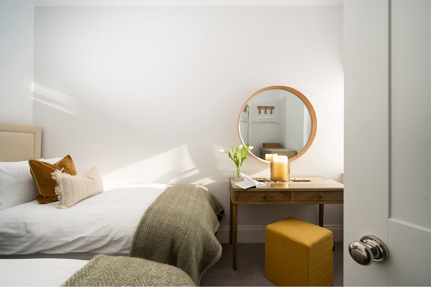 Light and calming twin bedroom with mustard and olive green accents, round mirror dressing table, natural textures and soft layering – styled by Iroka Interiors in St Ives.