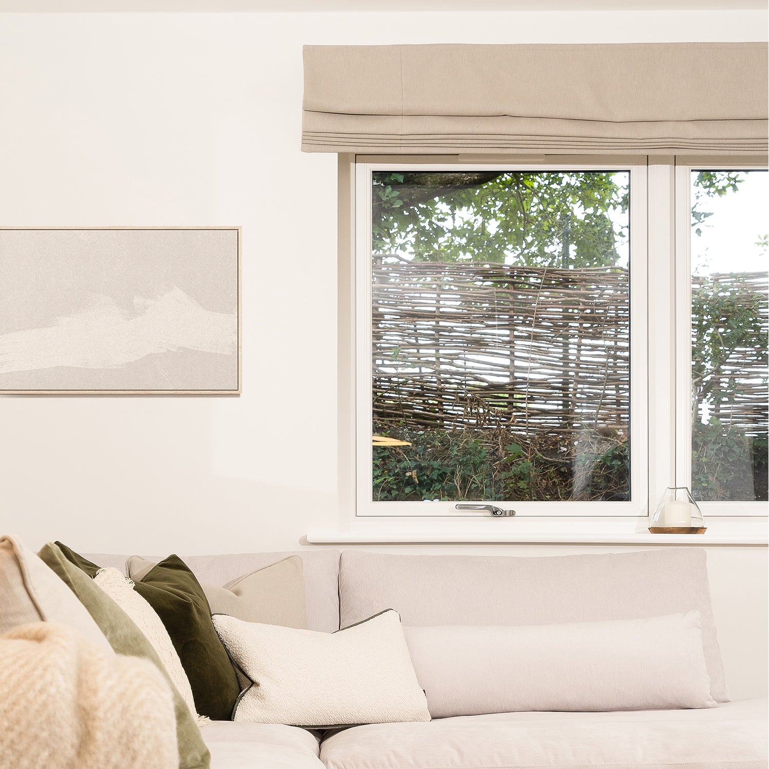 Neutral Roman blinds fitted in a light-filled living room with soft beige tones and bespoke upholstered sofa — handcrafted window treatments by interior design specialists.