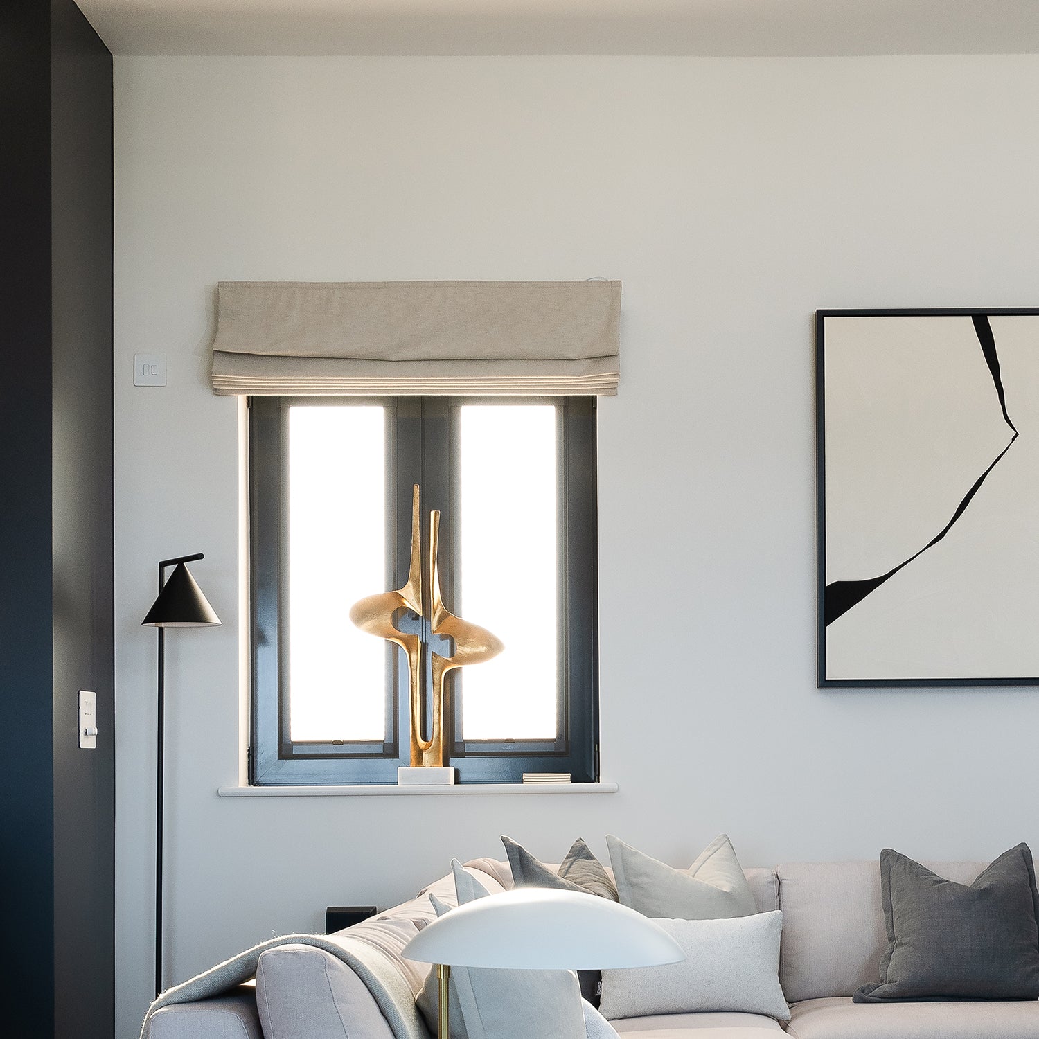 Contemporary living room featuring custom Roman blinds in neutral fabric, paired with modern monochrome décor and bespoke soft furnishings — tailored window treatments by interior design experts.