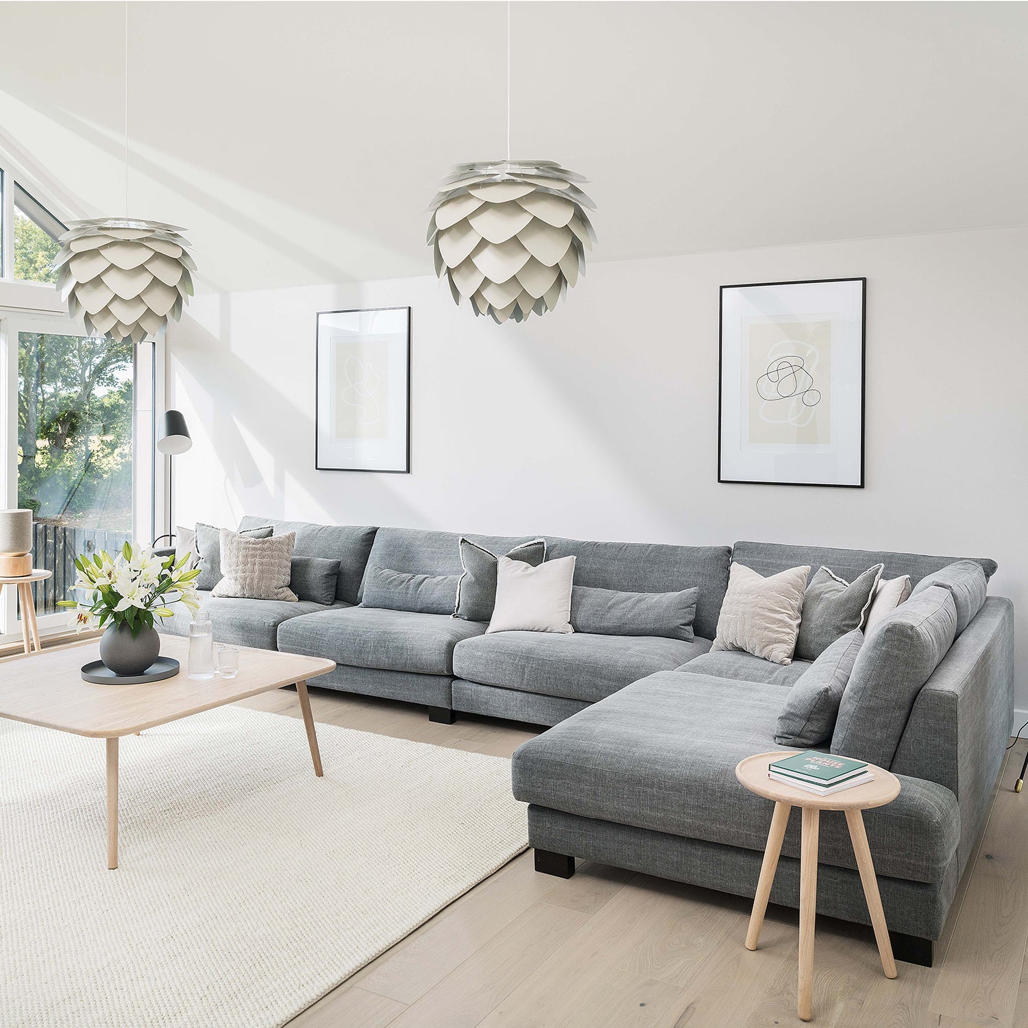 Modern coastal living room in Cornwall featuring a large grey corner sofa, Scandinavian-style light wood furniture, statement pendant lighting, and minimalist wall art – bespoke interior design and furniture by Iroka Interiors.