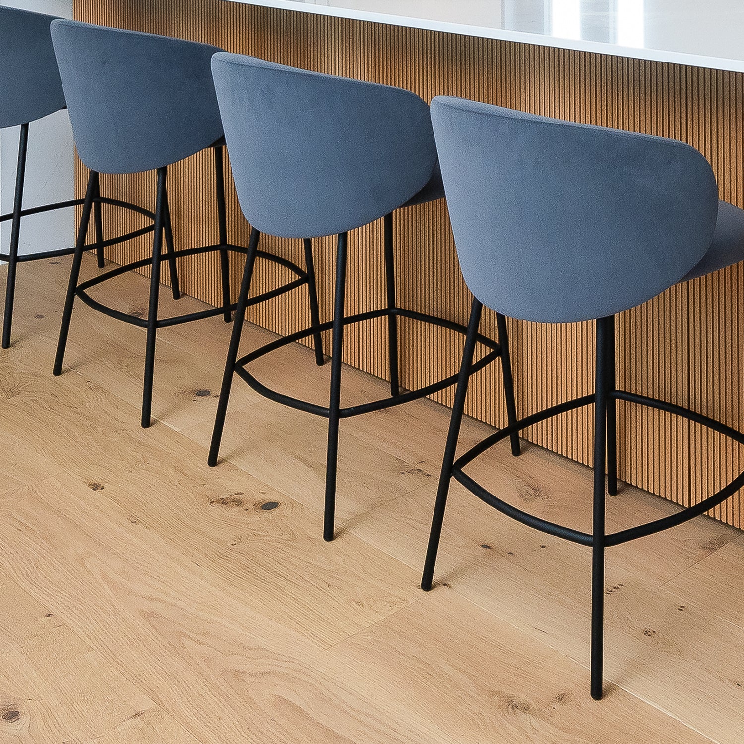 Contemporary oak wood flooring in a modern kitchen with stylish navy bar stools and fluted wood panel island – premium flooring by Iroka Interiors, Hayle Cornwall.