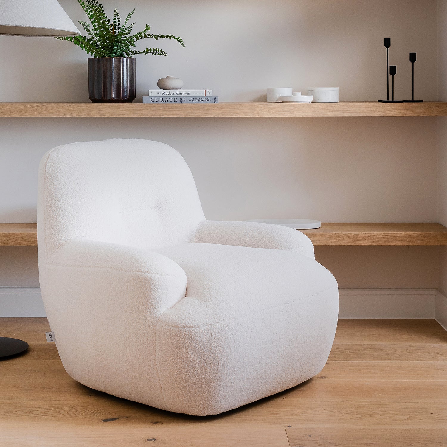 Modern lounge corner featuring a cream boucle armchair on light oak flooring, styled with floating wood shelves, minimalist decor, and neutral wall tones – cozy contemporary living room
