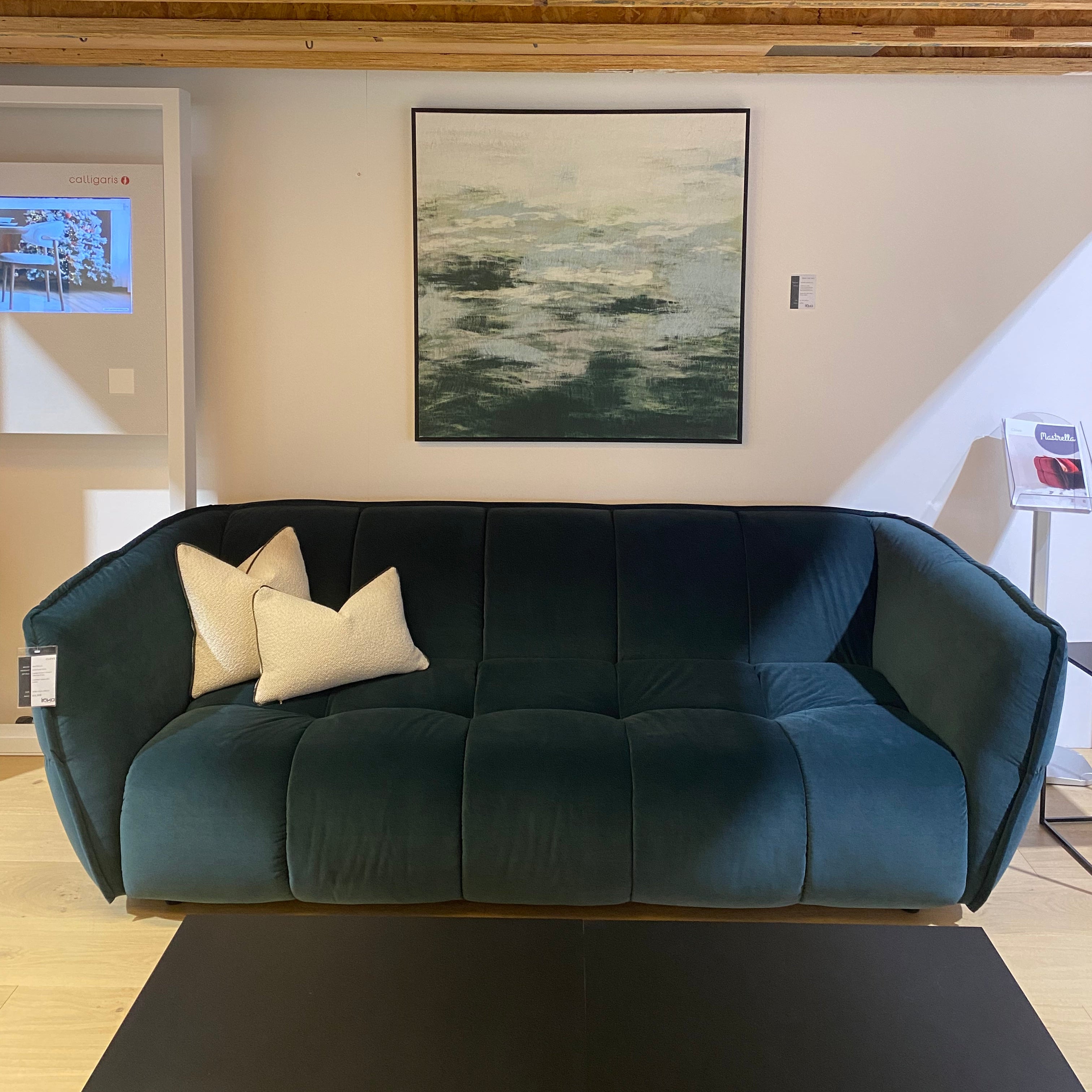 Green sofa with white cushions in a room with wooden walls and a painting on the wall.