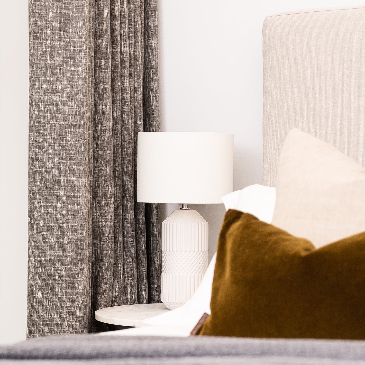 Elegant bedroom in Cornwall featuring bespoke full-length grey curtains, neutral headboard, and designer lighting – part of Iroka Interiors’ made-to-measure window dressing service.