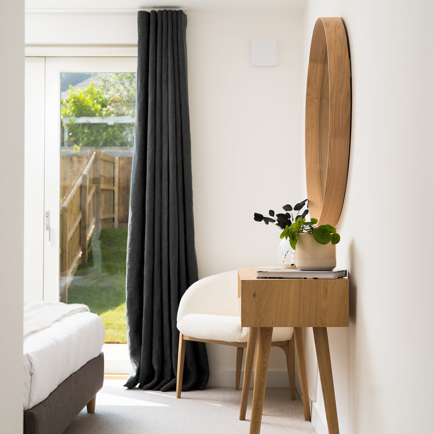 Contemporary bedroom with full-length charcoal curtains, wooden dressing table, and modern mirror—bespoke window treatment by Iroka Interiors in Cornwall.