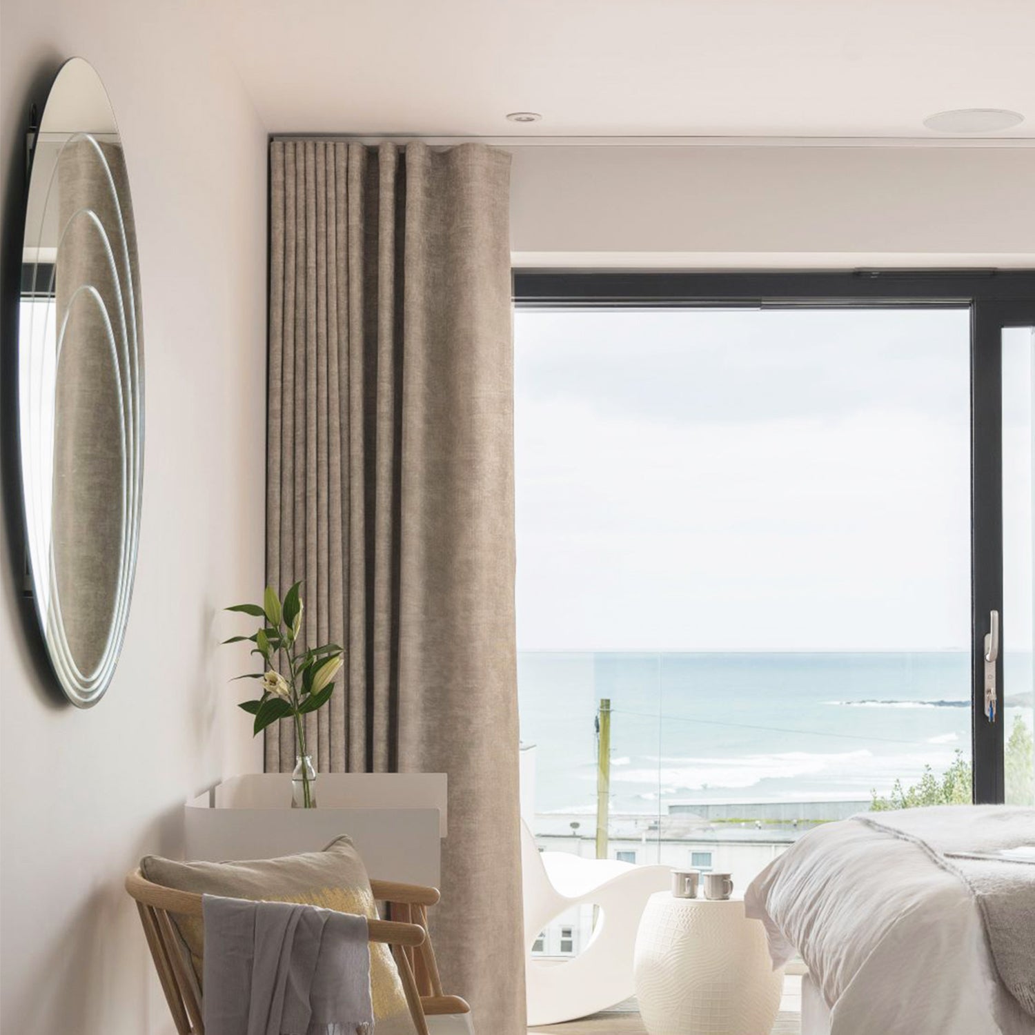 Elegant coastal bedroom with floor-to-ceiling bespoke curtains framing panoramic sea views, designed by a luxury interior design and window dressings specialist.