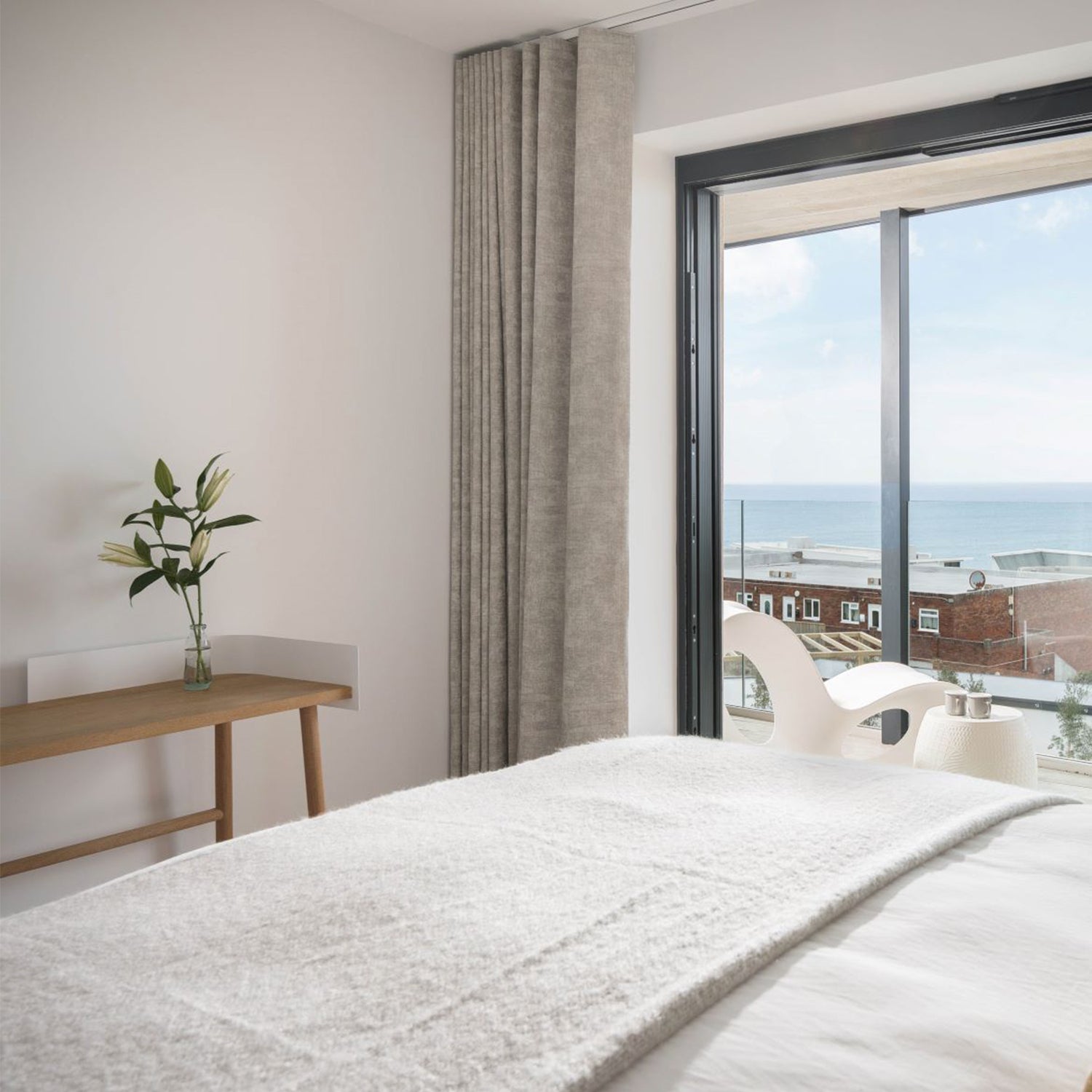 Contemporary coastal bedroom with floor-to-ceiling textured curtains framing a panoramic sea view, combining luxury design with light control.