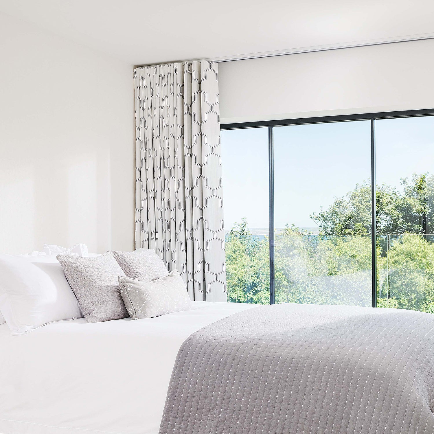 Bright modern bedroom featuring patterned full-length curtains paired with sleek white blackout blinds, offering a stylish and functional window dressing solution.