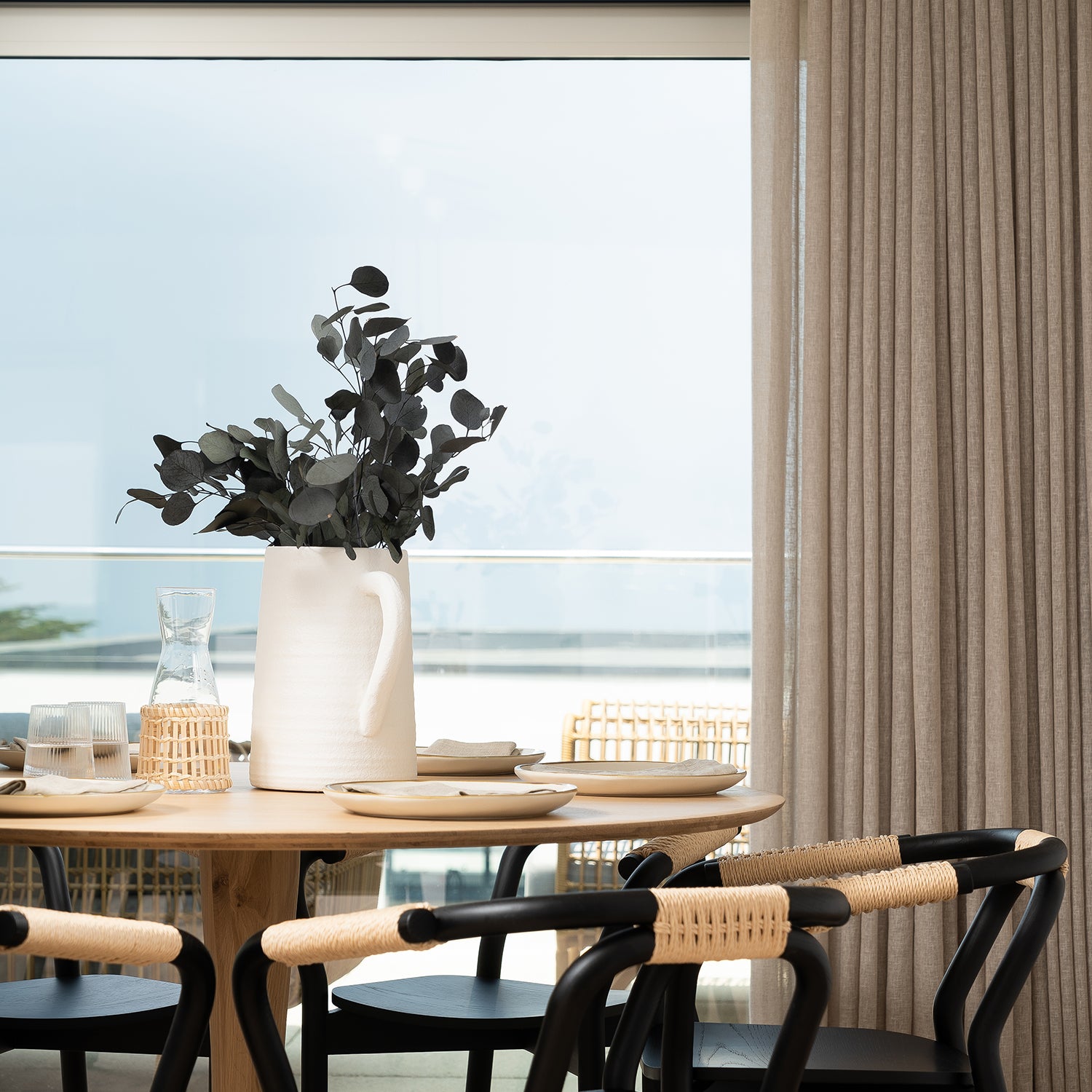 Elegant floor-to-ceiling linen curtains framing a sea-view dining area with Scandinavian-style furniture — bespoke window treatments by luxury interior design studio.