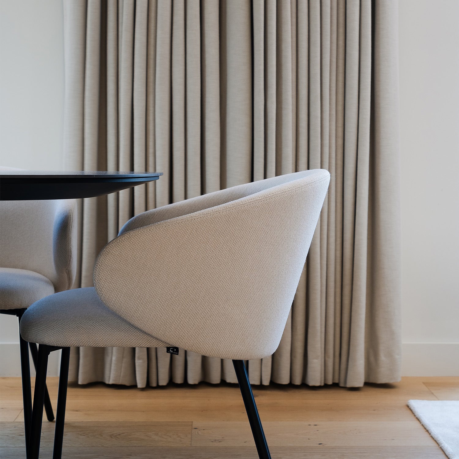 Elegant dining area featuring modern beige upholstered dining chair with black legs, soft floor-to-ceiling taupe curtains, and light wood flooring – minimalist interior design and curtain styling inspiration.
