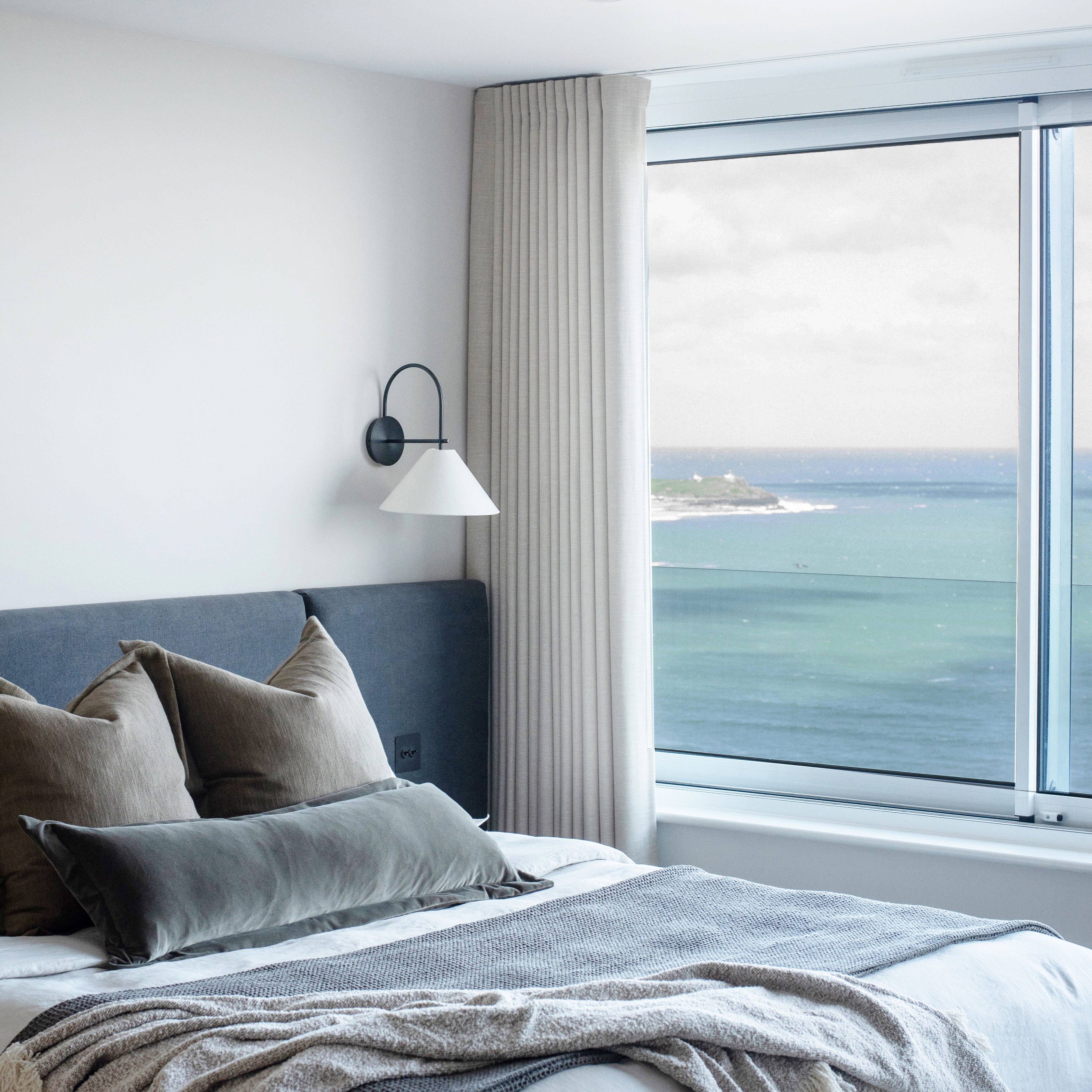 Modern coastal bedroom view of St Ives with floor-to-ceiling sheer curtains by Iroka, framing panoramic ocean views and softening natural light.