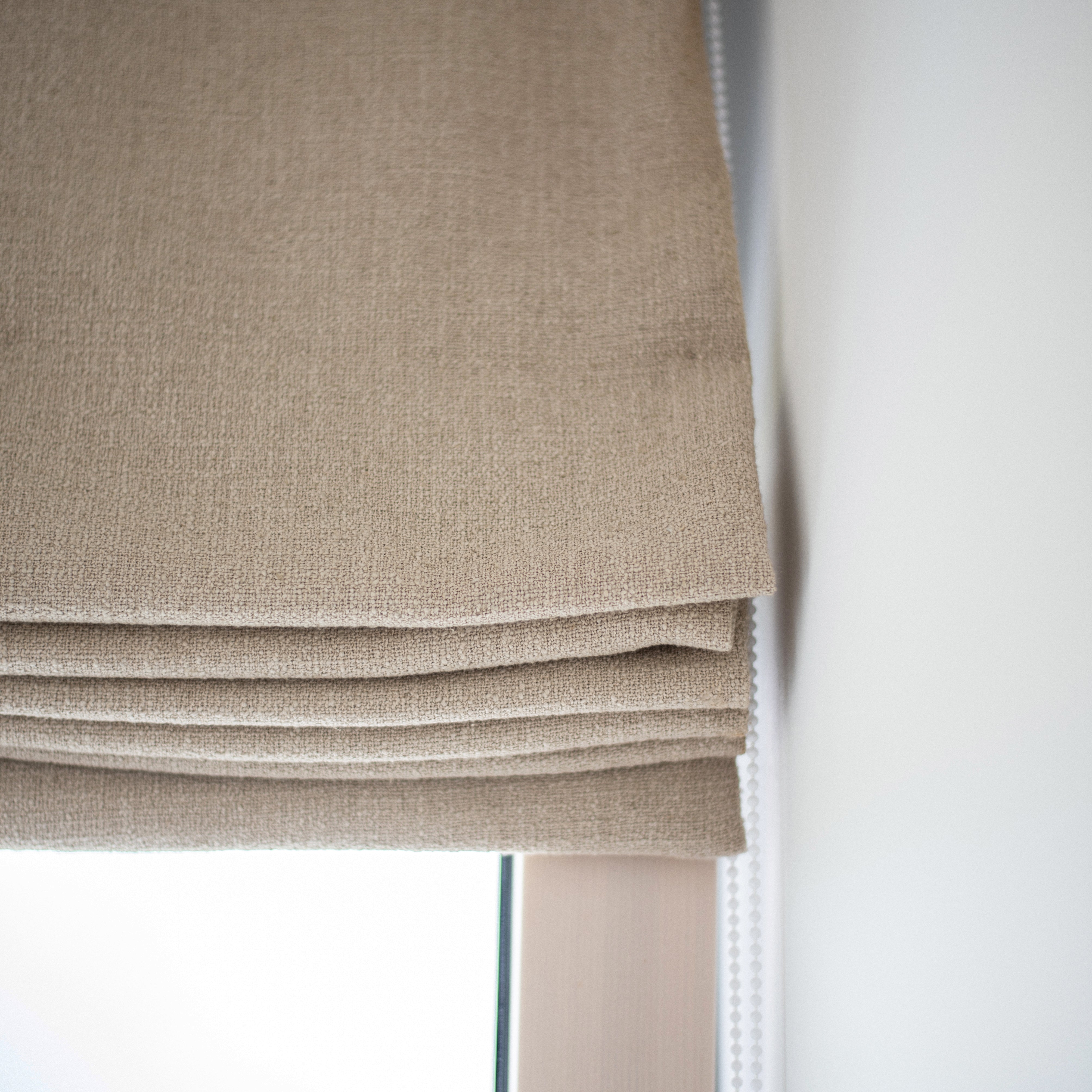 Close-up of a textured neutral Roman blind with chain mechanism, handcrafted by Iroka Interiors in Cornwall, highlighting premium bespoke window dressing solutions.