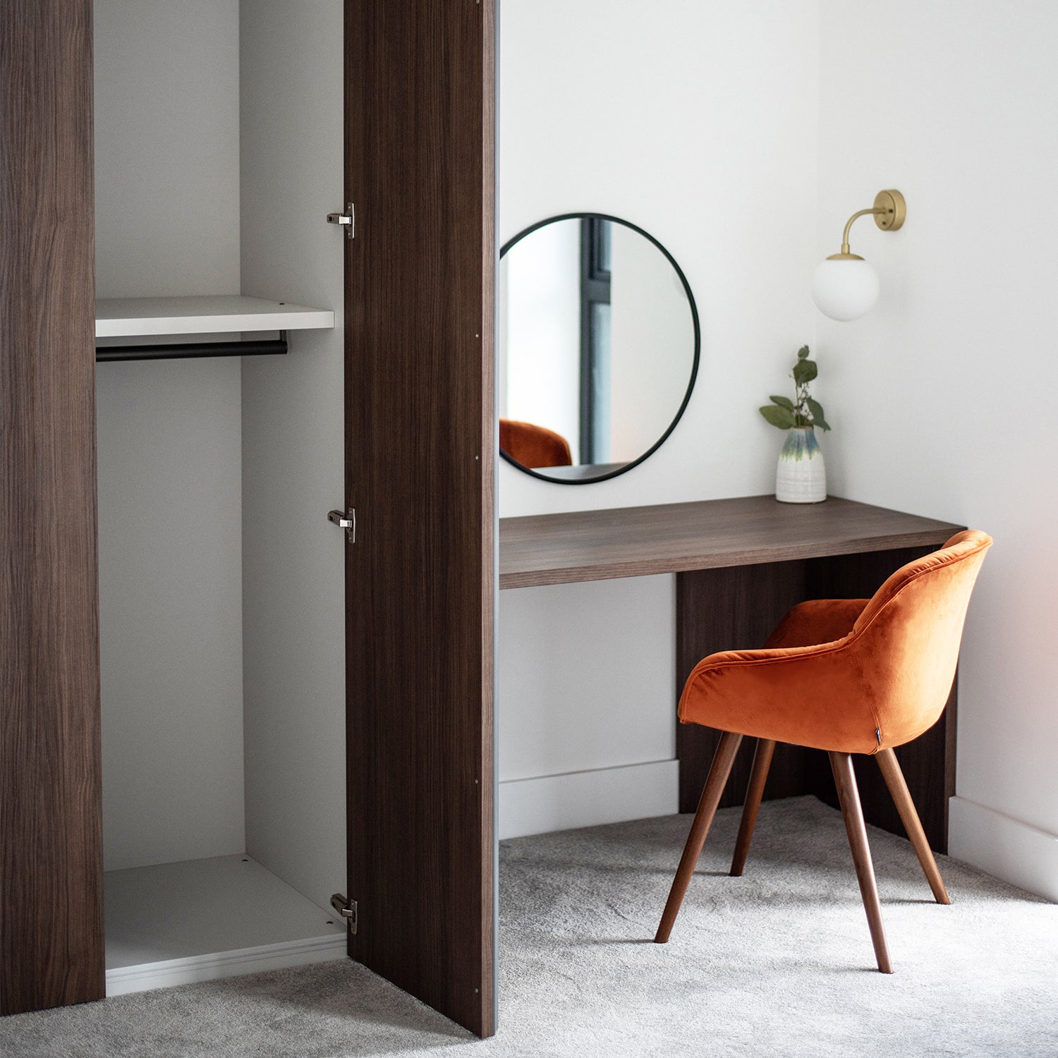 Modern bedroom corner with walnut wood built-in wardrobe, minimalist dressing desk and round wall mirror, paired with a plush burnt orange velvet chair – Penhalls Drive, Playing Place.