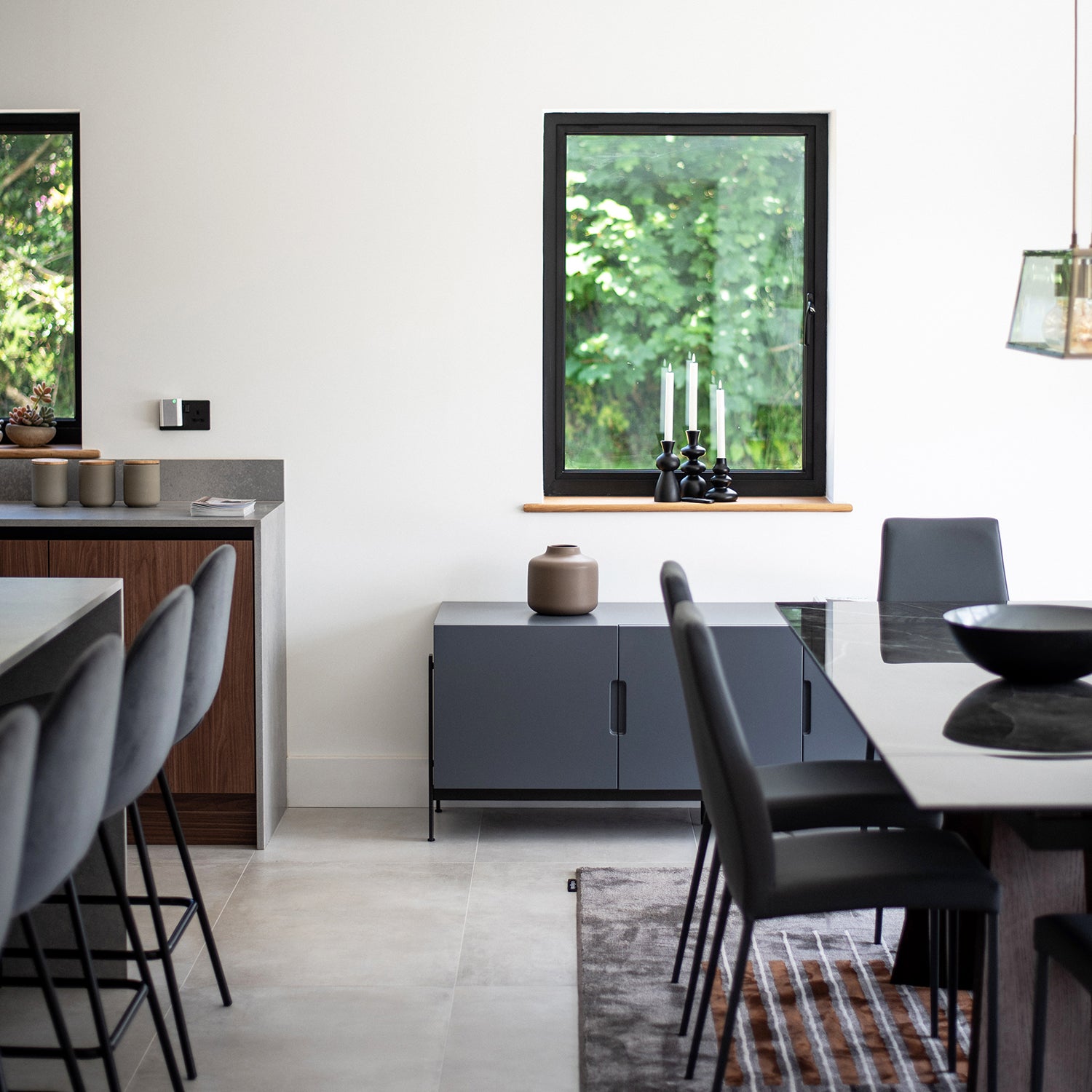 Modern open-plan dining and kitchen area featuring black dining chairs, grey cabinetry, minimal décor – interior design by Iroka, Playing Place, Truro.
