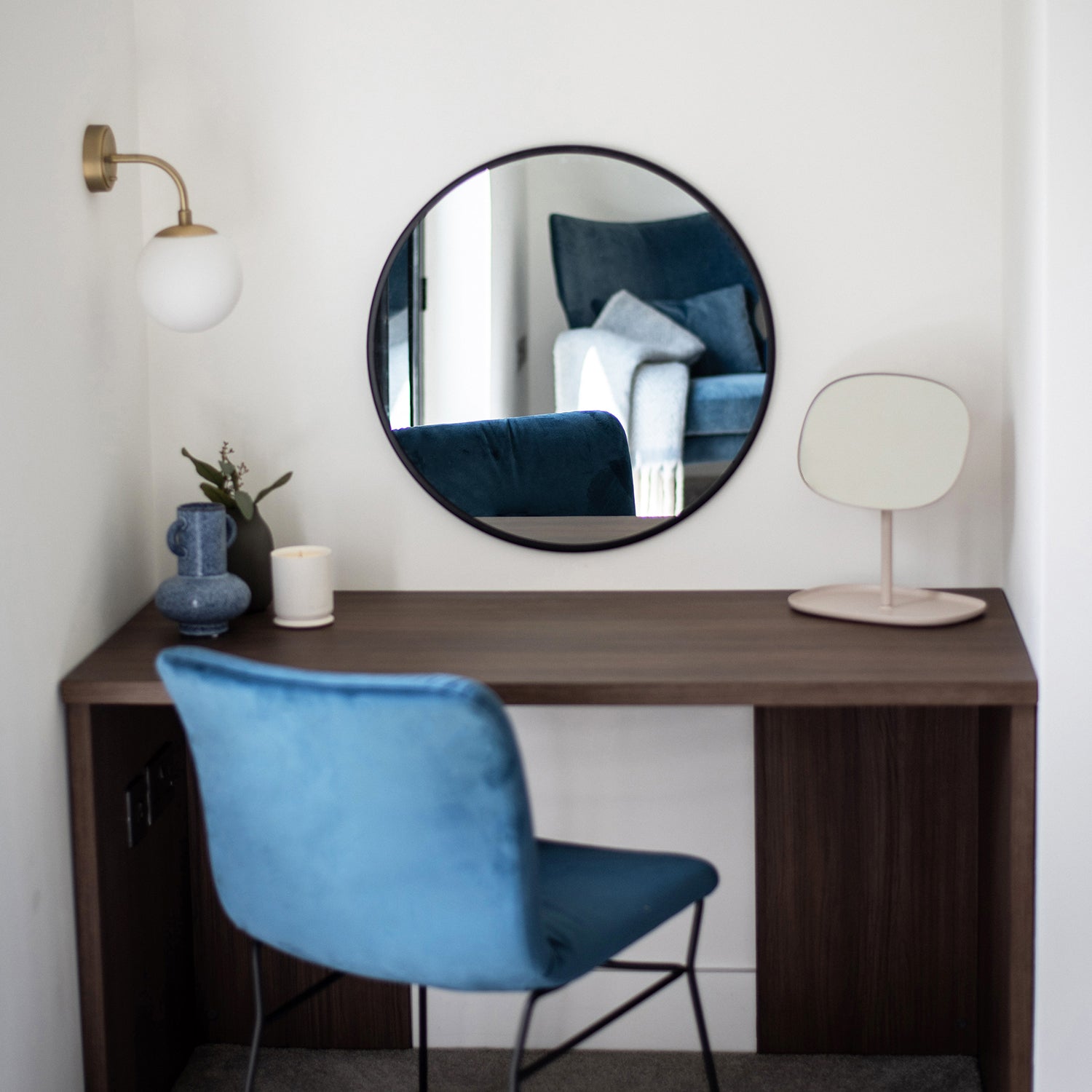 Contemporary dressing table with walnut wood finish, round mirror, blue velvet chair, and modern accessories in a stylish bedroom nook – designed by Iroka Interiors.