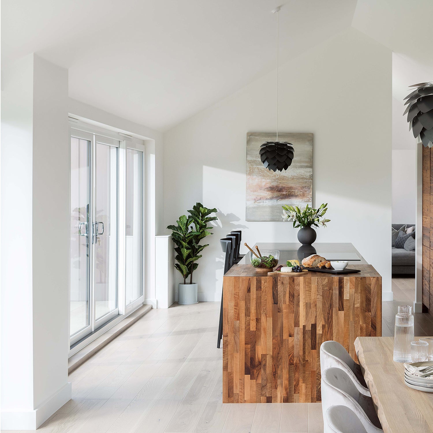 Bright modern kitchen with pale oak wood flooring, natural light from sliding glass doors, wooden island centerpiece, and minimalist décor for a Scandinavian-inspired interior.