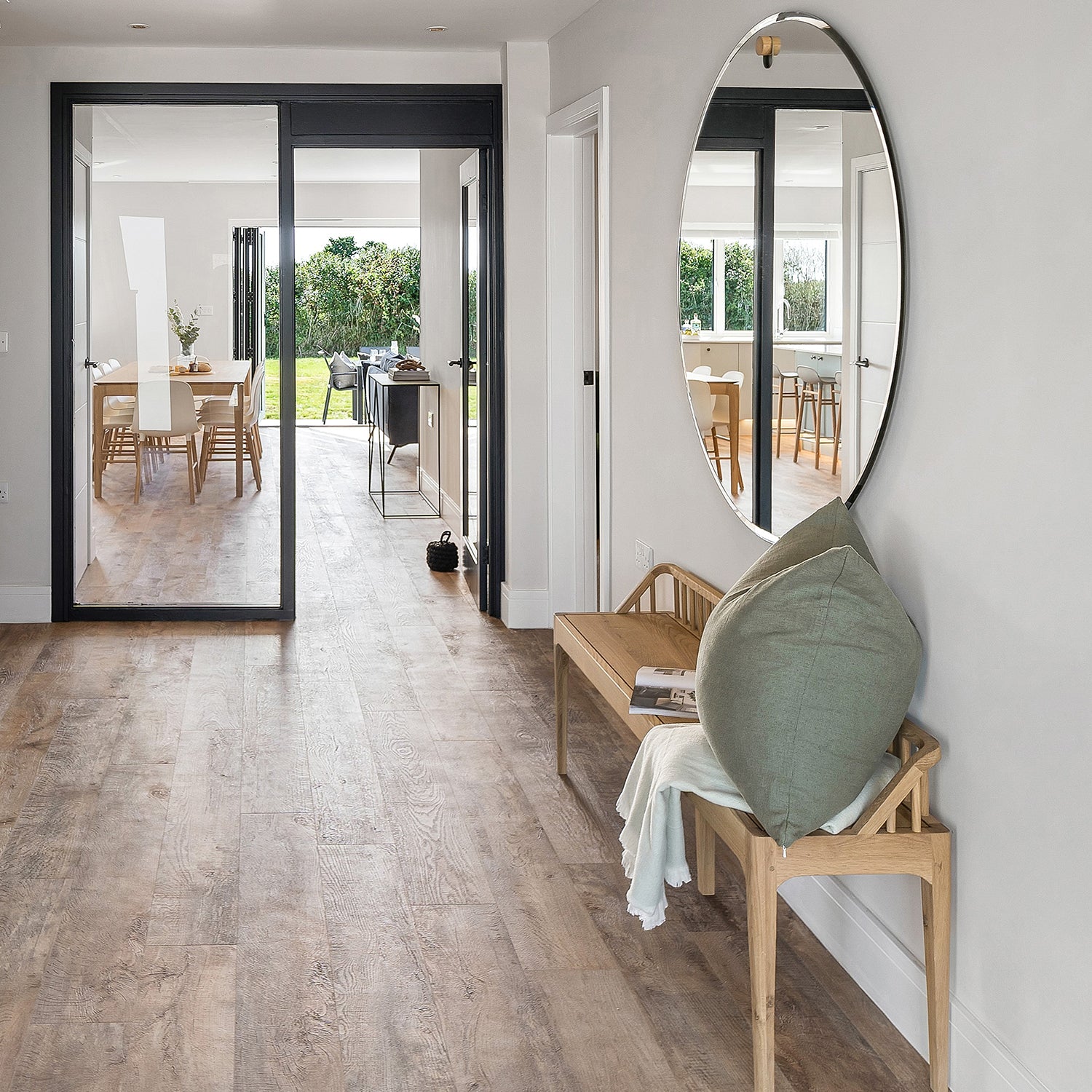 Warm wood-effect luxury vinyl tile flooring in a bright contemporary hallway and dining area, styled with minimalist furniture, neutral tones, and natural light for a modern and welcoming interior.