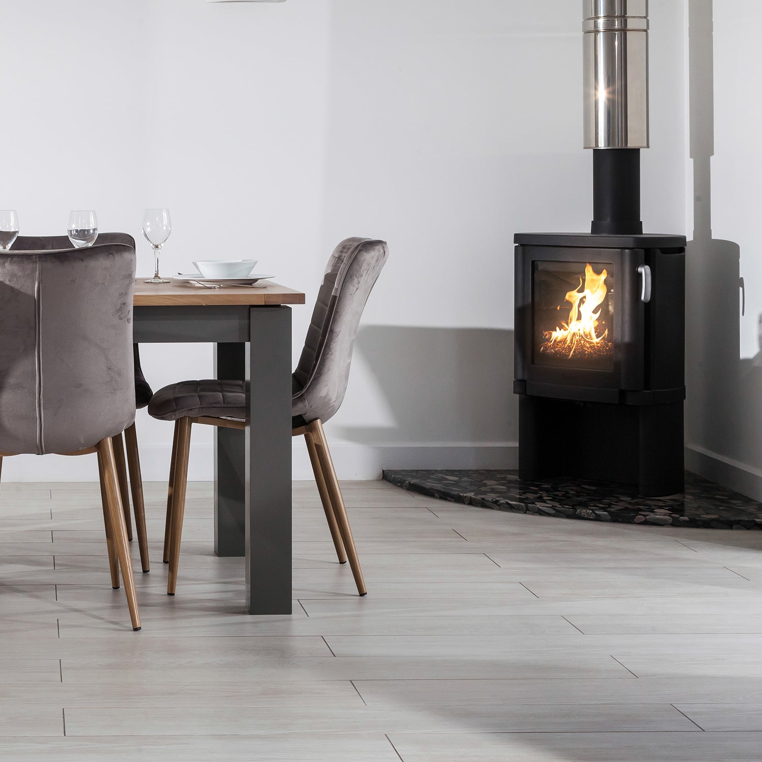 Modern dining room with pale luxury vinyl flooring and contemporary wood-burning stove on a slate hearth – durable and stylish flooring by Iroka Interiors.