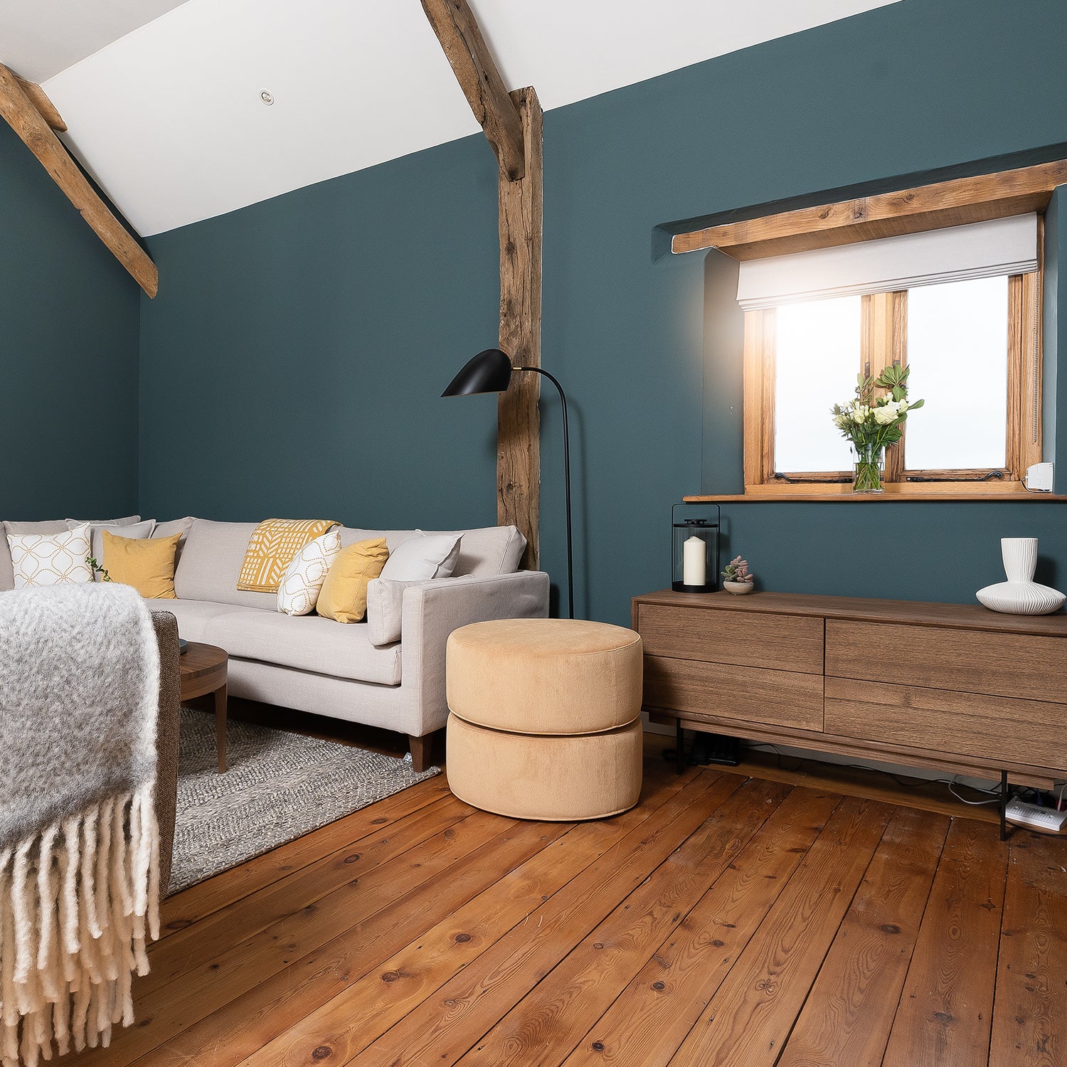 Rustic solid wood flooring in a cosy modern living room with exposed beams, teal feature wall, light grey sofa, and natural oak accents, creating a warm and inviting atmosphere.