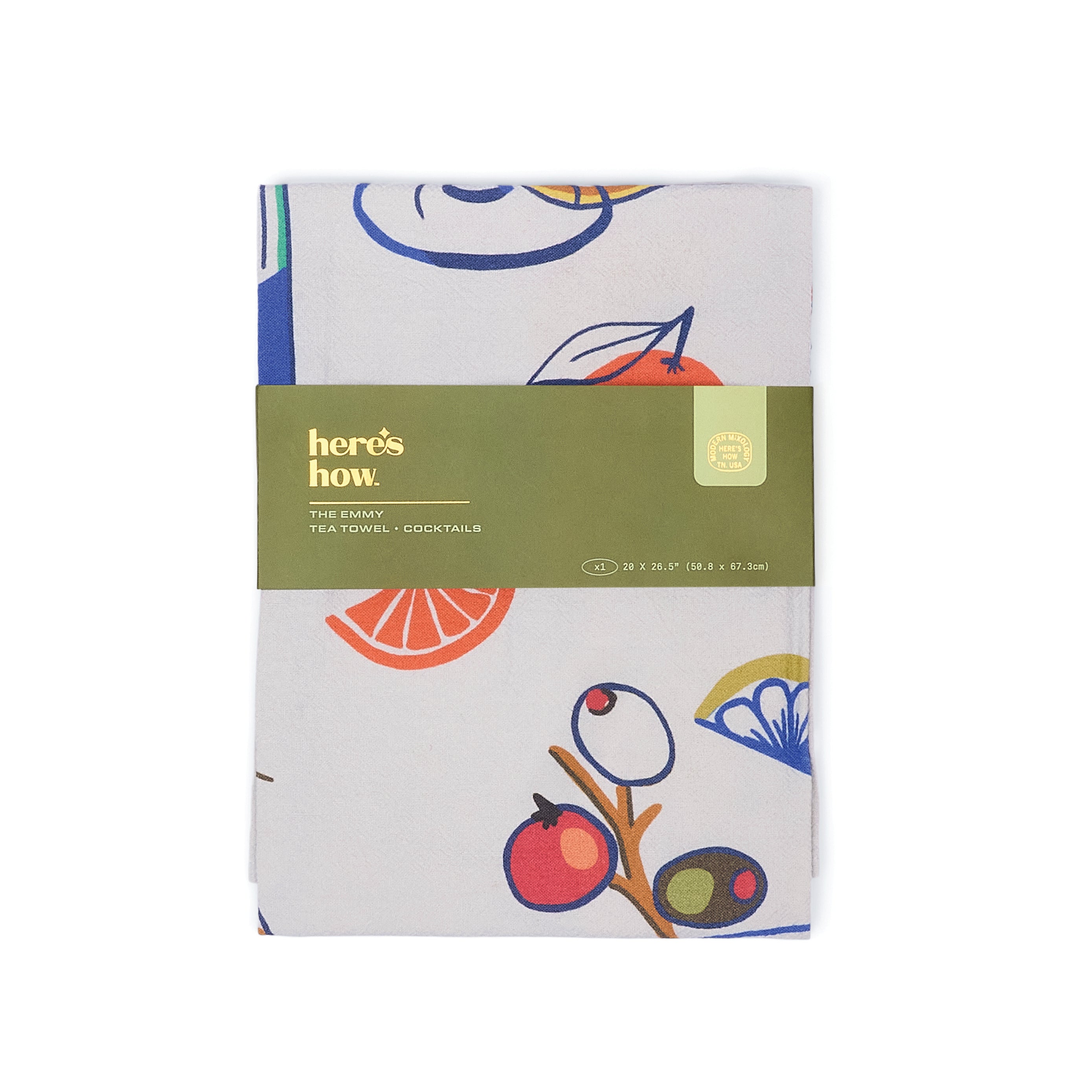 A folded white tea towel with a colourful fruit, cocktail pattern, wrapped in a green paper band that reads 'here's how. THE EMMY TEA TOWEL + COCKTAILS'.