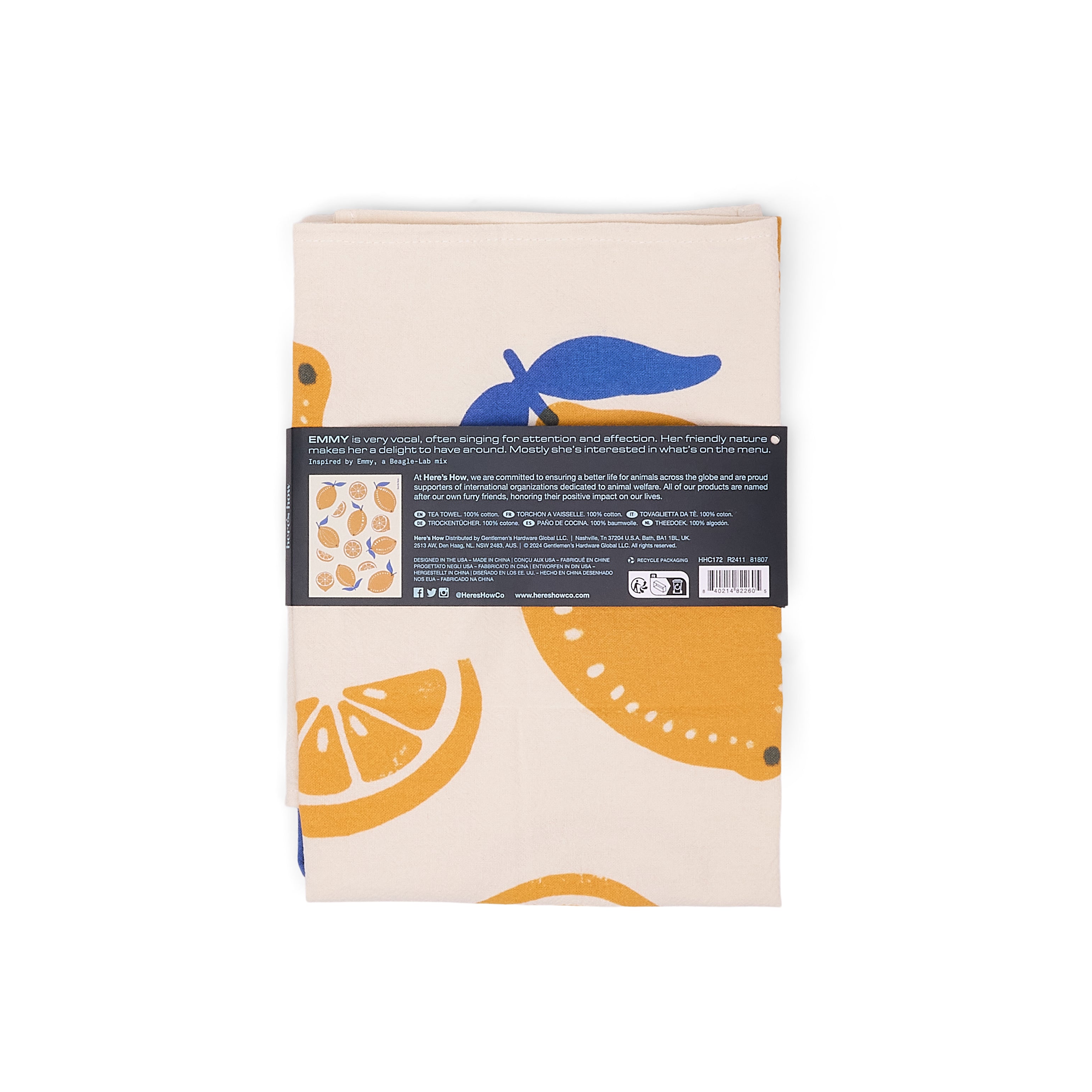 A folded cream-colored tea towel with a lemon pattern, wrapped in a black paper band with product details.