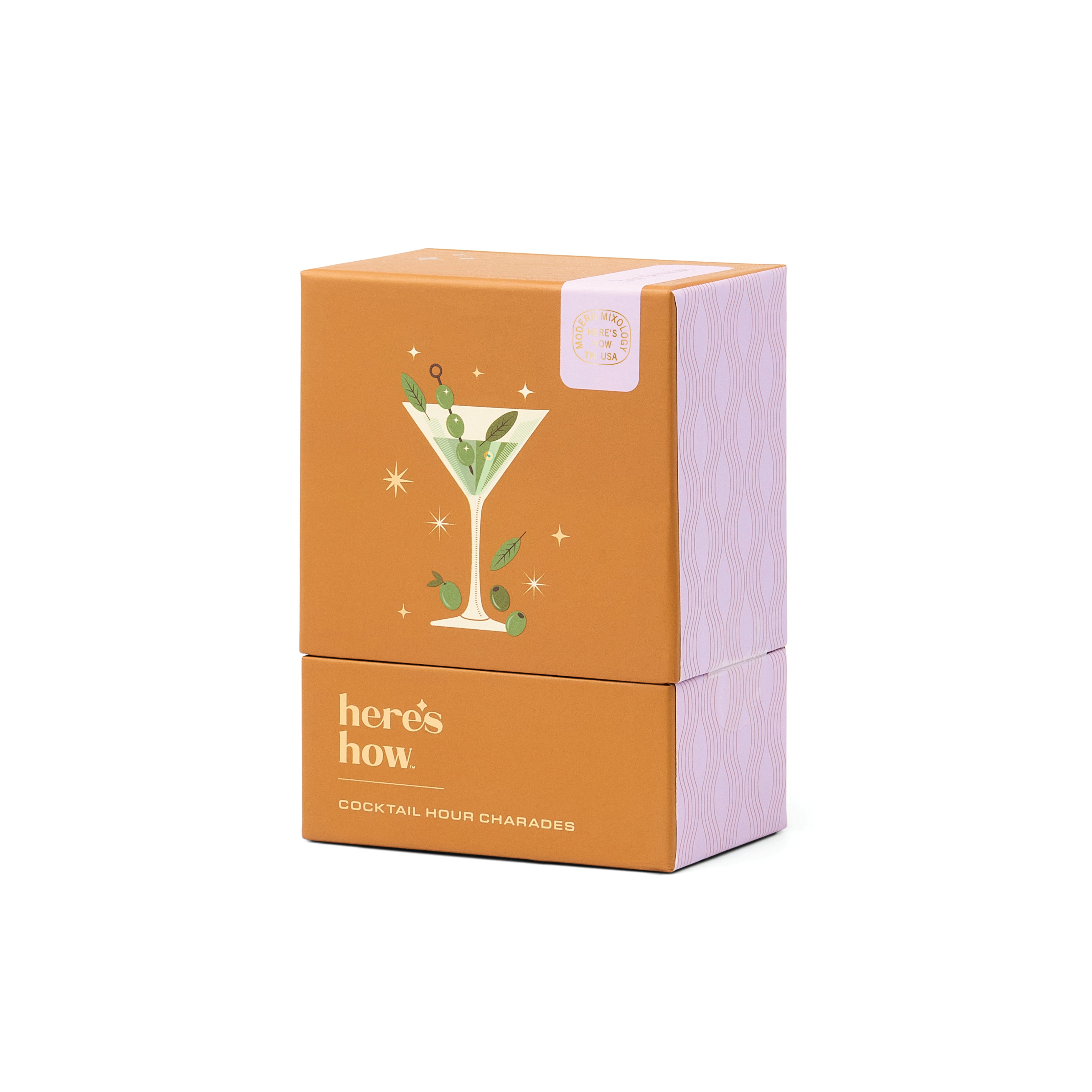 A stacked cardboard box of 'here's how' Cocktail Hour Charades, featuring an orange front with a martini glass illustration and white text, and lavender patterned sides, set against a plain white background.