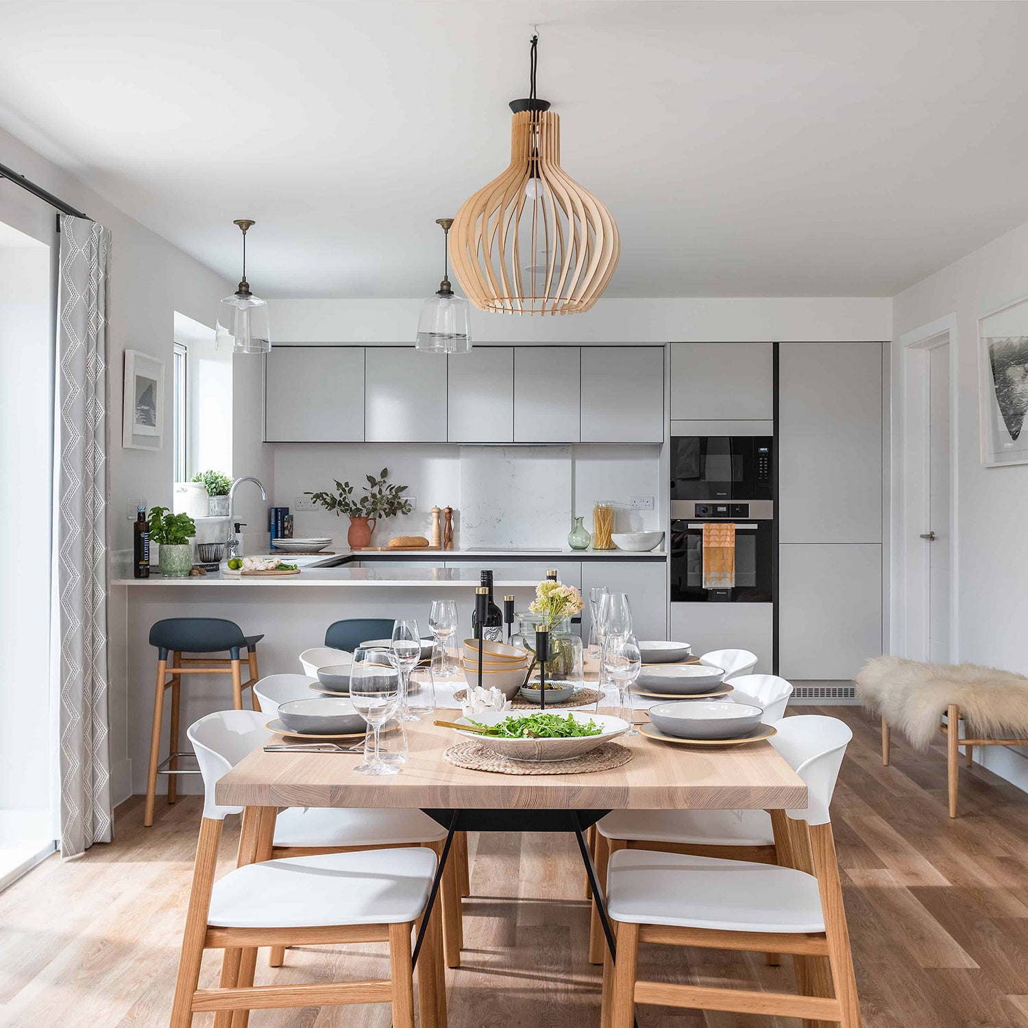 Bright and modern open-plan kitchen and dining area in Cornwall featuring white cabinetry, oak dining table, Scandinavian chairs, and pendant lighting – bespoke home interiors and furniture by Iroka Interiors.