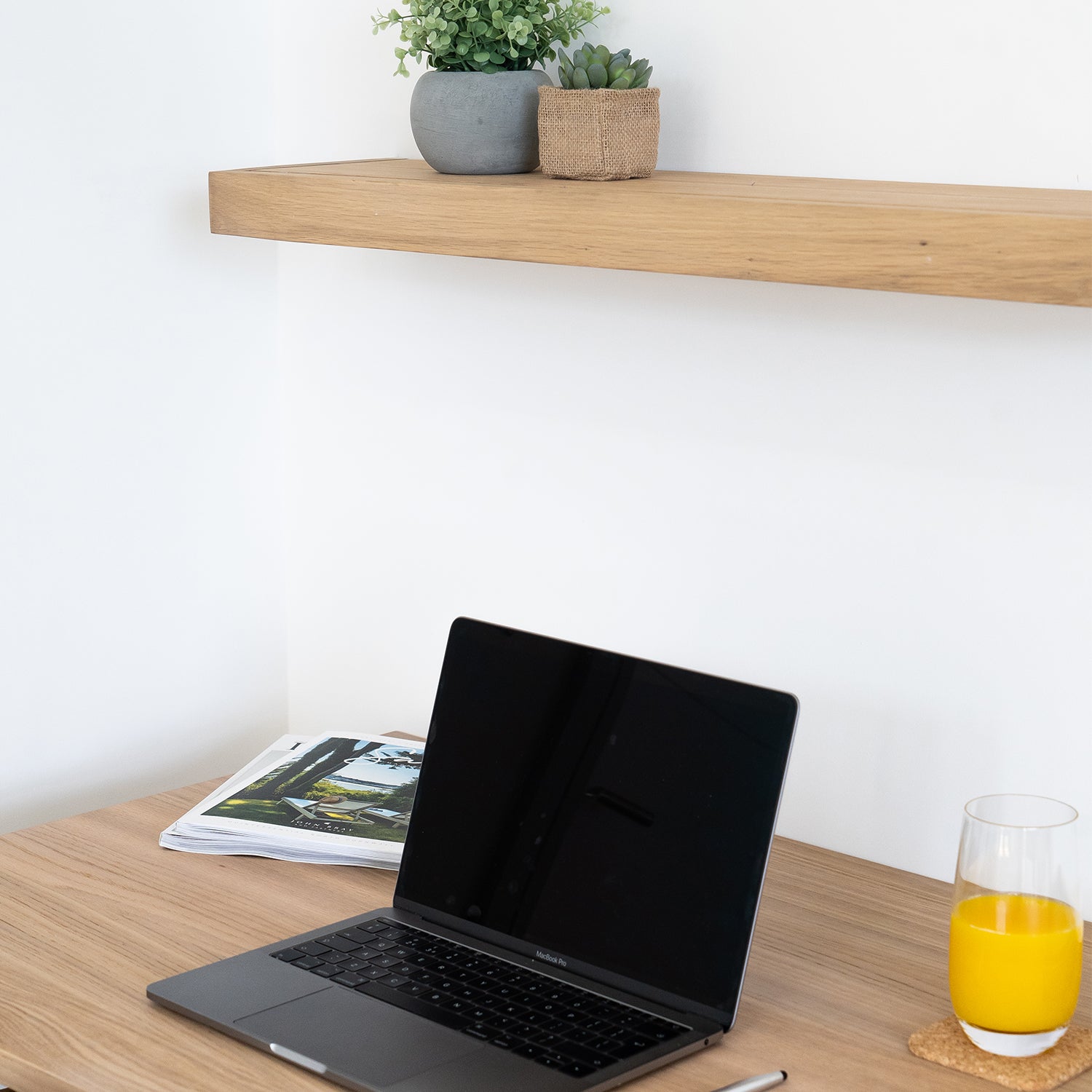 Minimalist hotel workspace designed by Iroka Interiors in Cornwall, featuring a natural oak desk with a floating shelf, potted succulents, MacBook laptop, and a fresh glass of orange juice – perfect for modern hospitality design and remote working amenities.