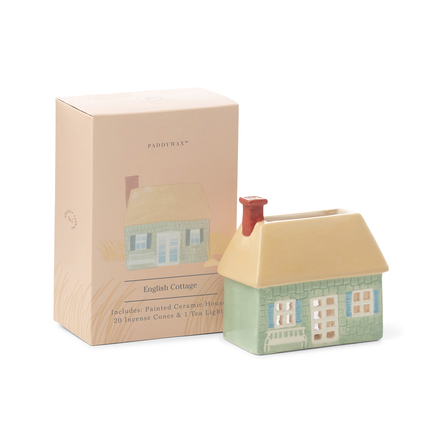 A beige and green ceramic incense and tea light holder in the shape of an English cottage, placed next to its pink box with the product name and image of the cottage on it.