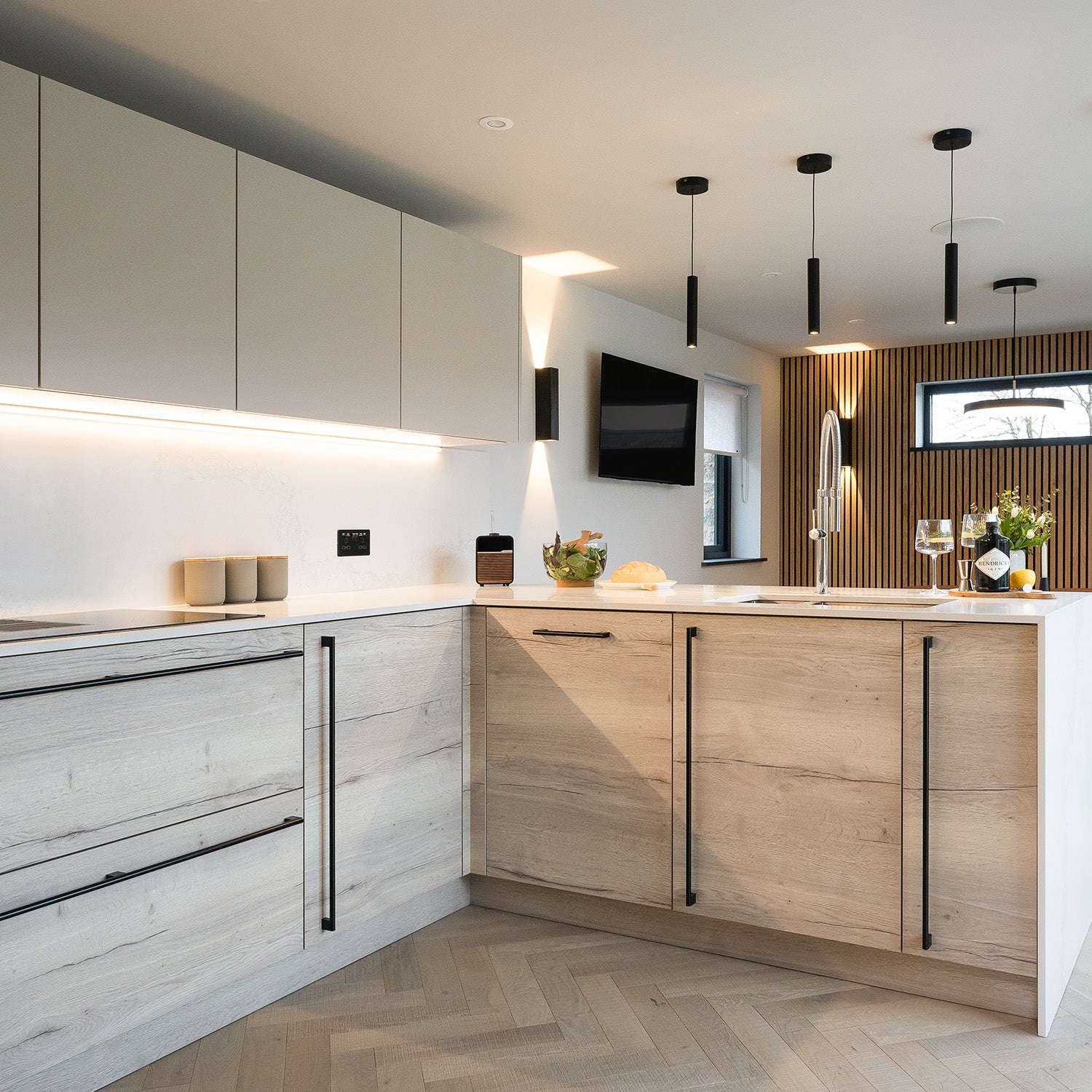 Contemporary open-plan kitchen with light wood and matte grey cabinets, integrated appliances, pendant lighting, and herringbone flooring – modern kitchen design inspiration for minimalist interiors.