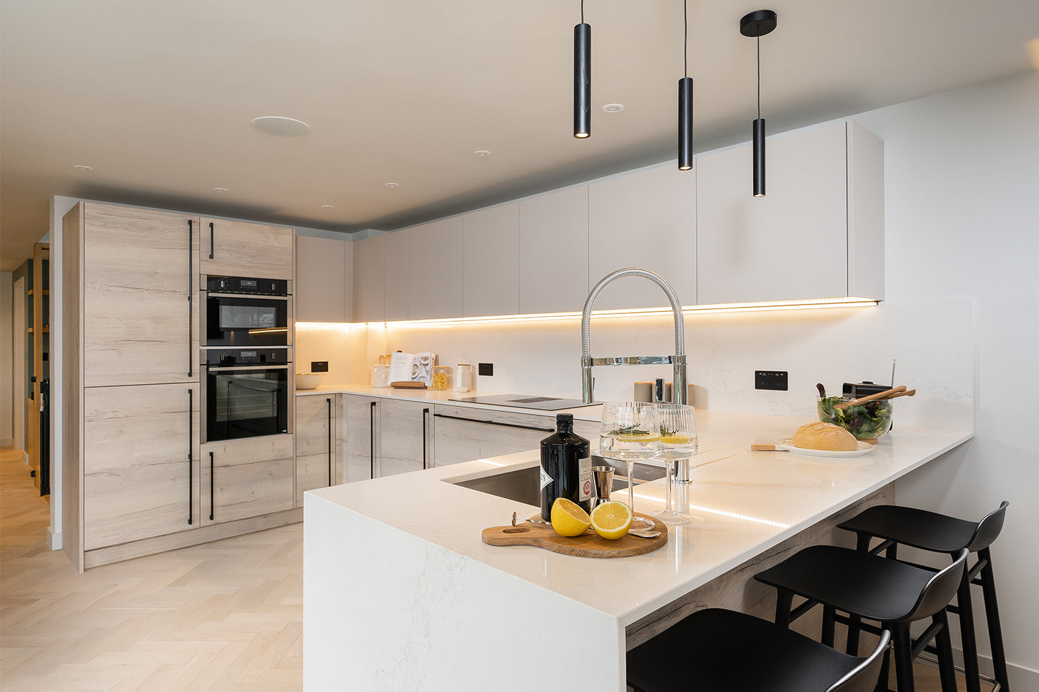 Luxury modern kitchen with white handleless cabinetry, LED under-cabinet lighting, quartz island with breakfast bar, and integrated appliances – bespoke kitchen design and installation by Iroka Interiors Cornwall