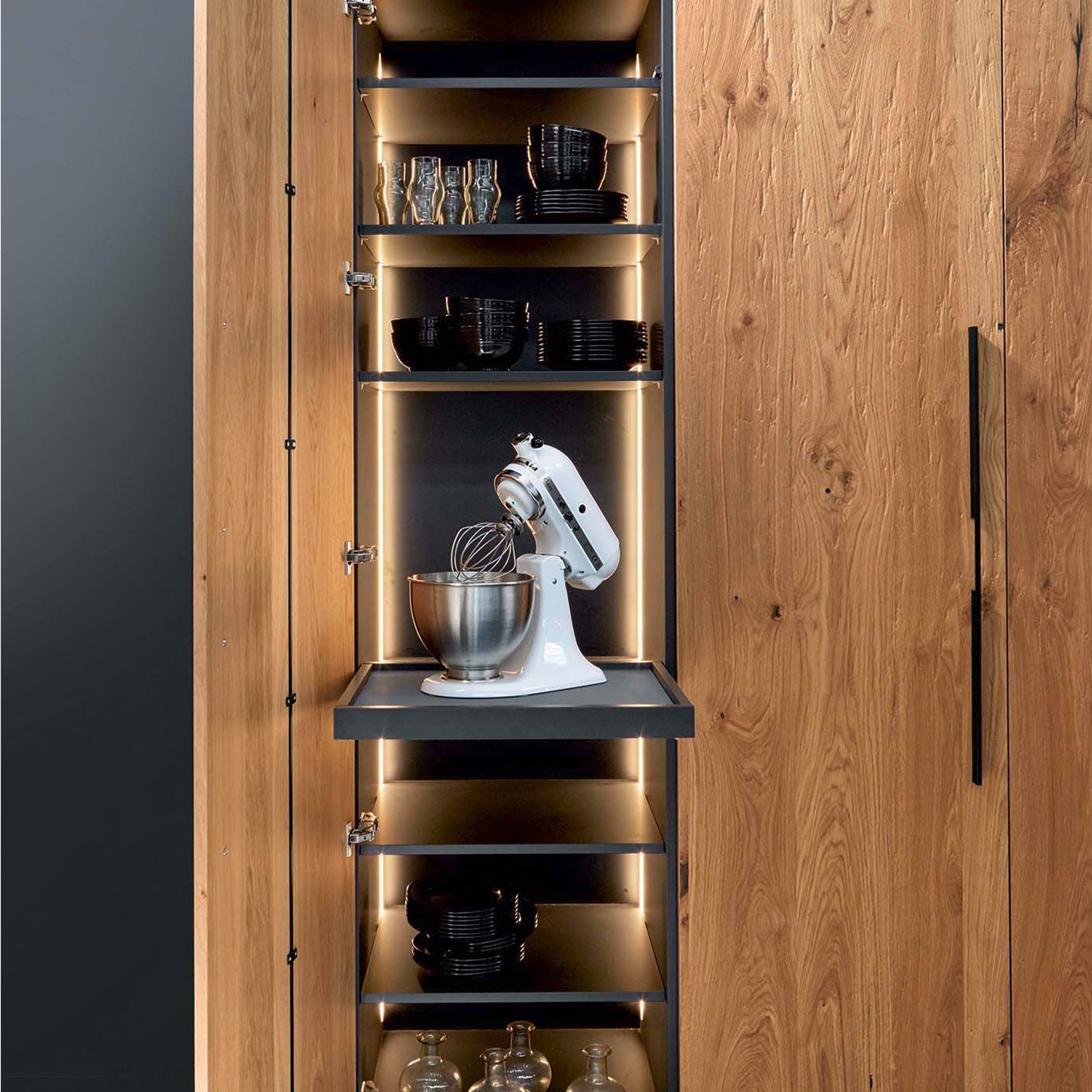 Bespoke kitchen storage solution with integrated oak larder cabinet, LED-lit shelving, and pull-out platform for stand mixer – modern space-saving design by Iroka Interiors Cornwall.