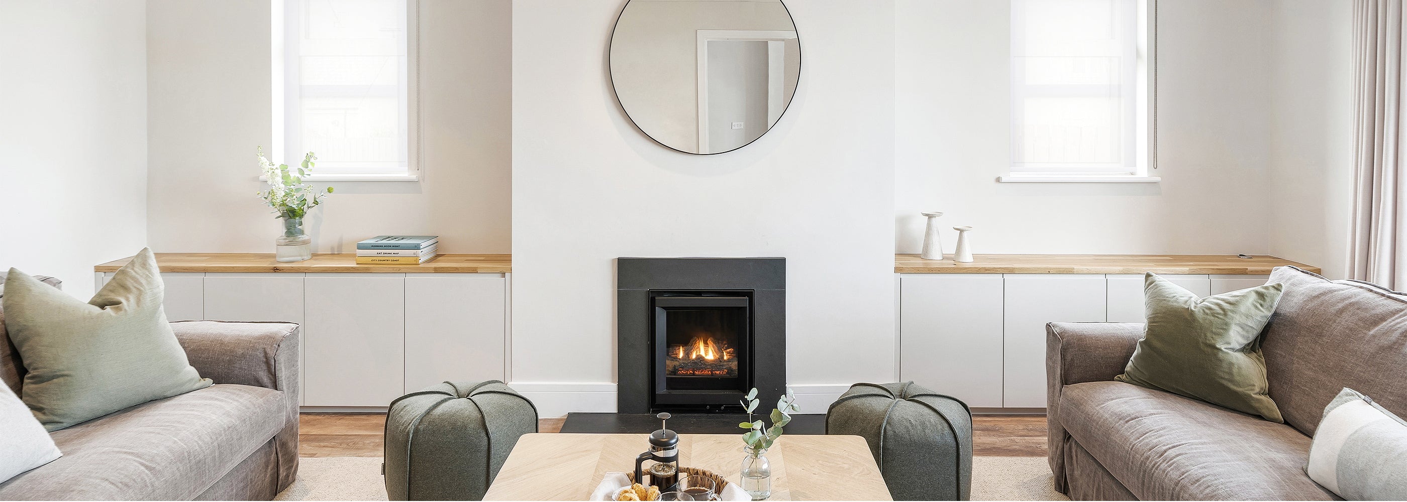 Elegant living room setting in a luxury furniture showroom featuring a modern fireplace, bespoke white cabinetry, natural wood accents, and a mix of neutral-toned sofas and armchairs with plush cushions — showcasing timeless interior design.