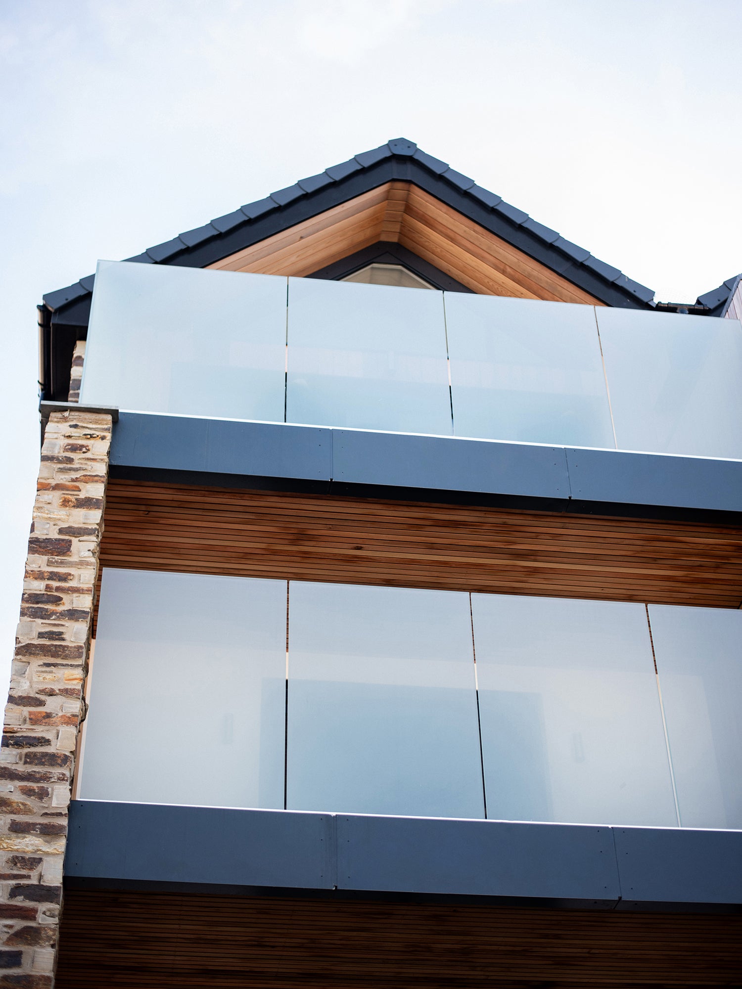 Modern coastal home exterior with glass balconies, timber cladding, and pitched roof detailing with contemporary architecture.